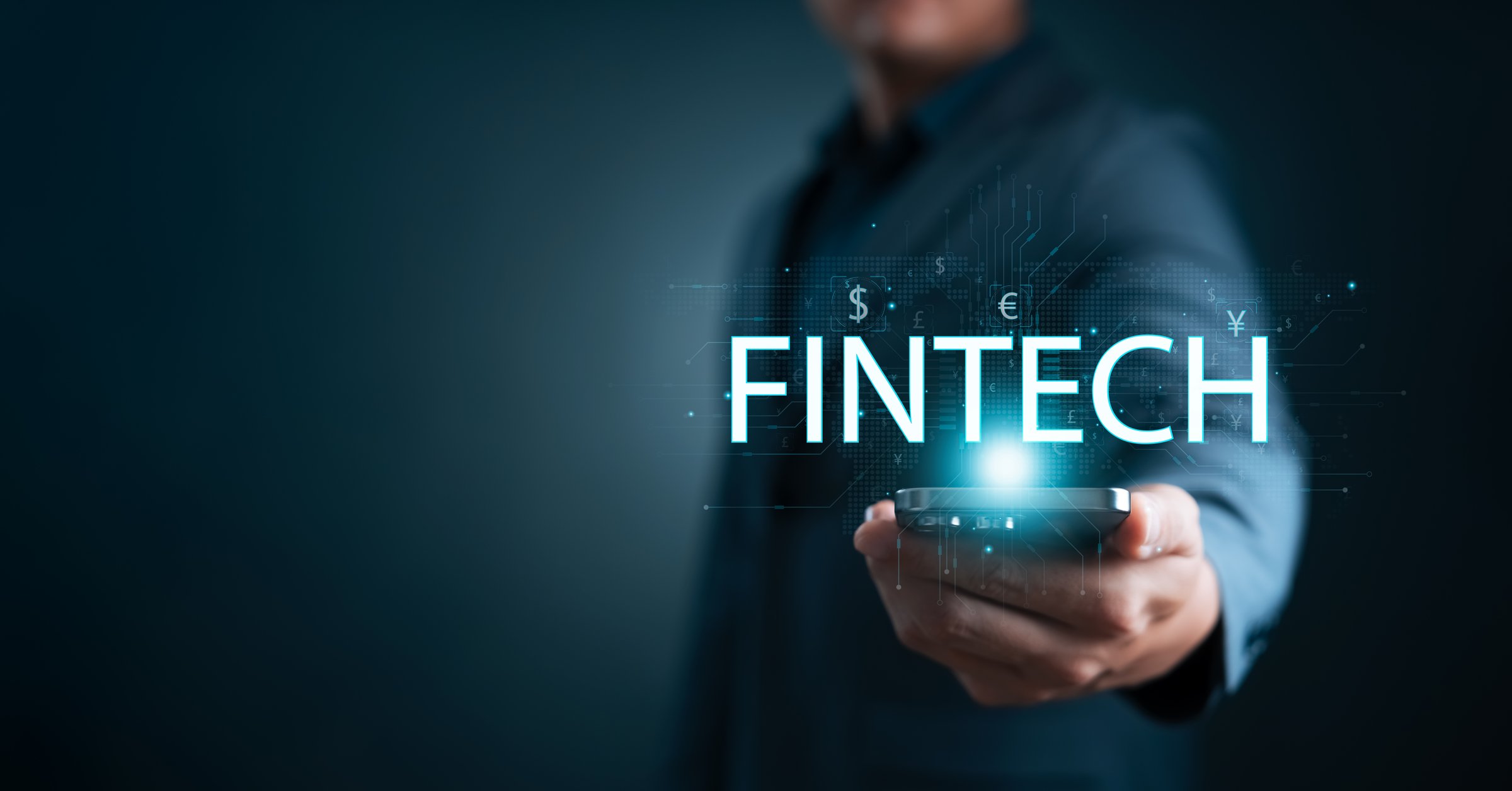 Businessman holding smartphone with glowing FINTECH text and currency symbols, representing digital finance, financial technology, innovation, online banking, and future economy.