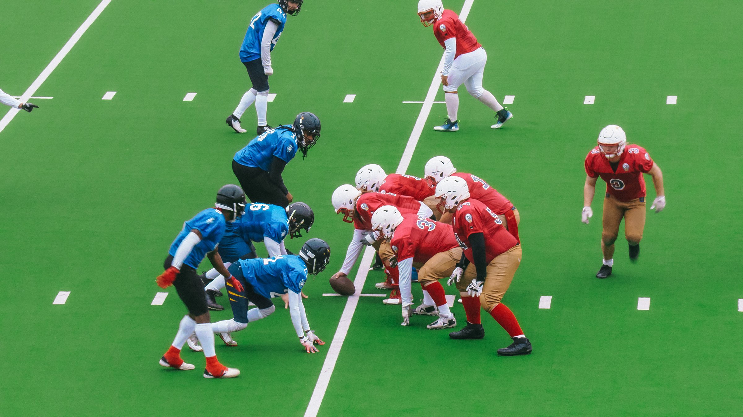 Two American Football Teams Stand Across From Each Other on the Line of Scrimmage as the Ball is Ready to be Passed to Start the Game. Gridiron Players Ready to Tackle and Defend
