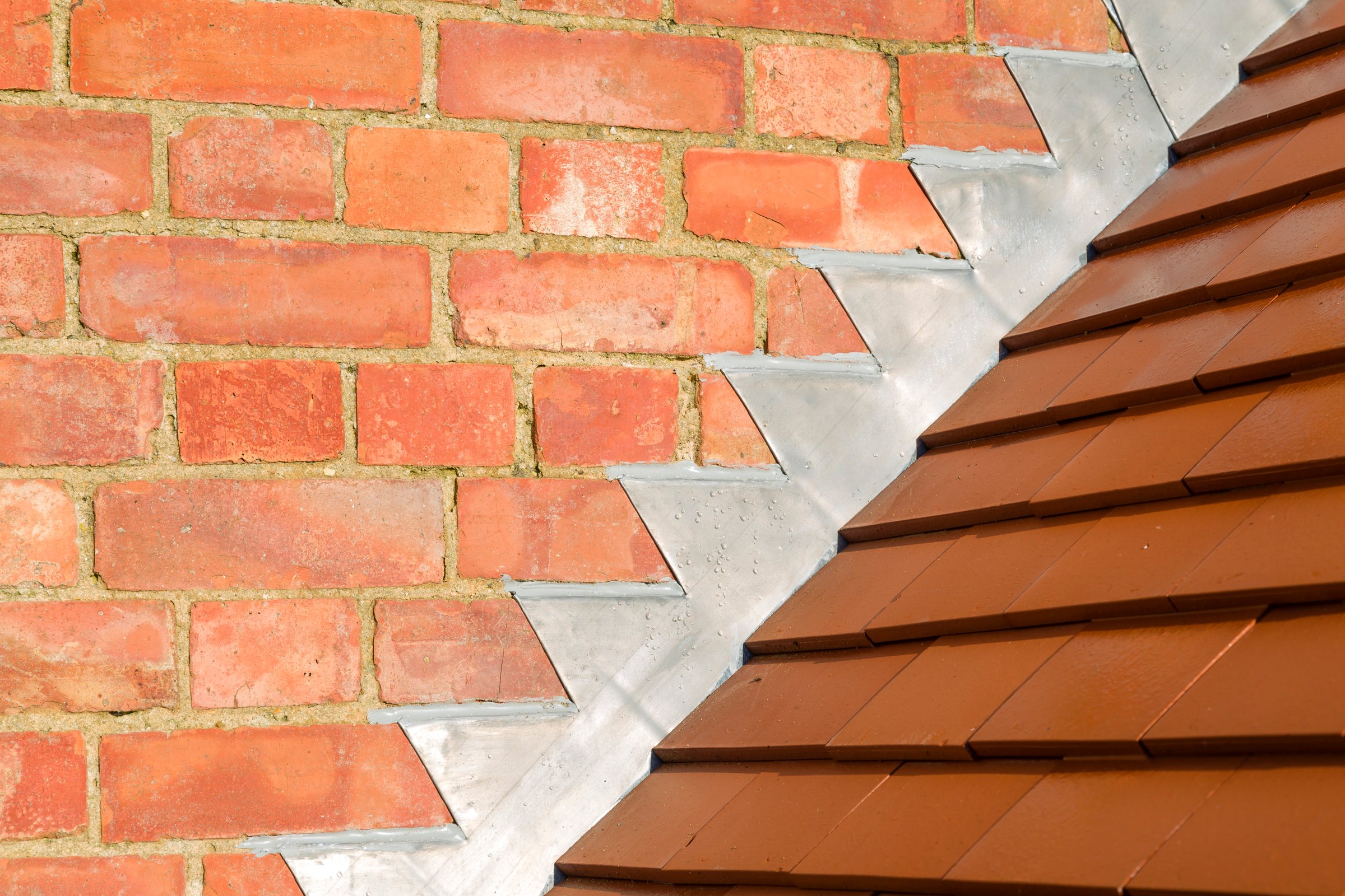 Closeup of new plain red clay tiles and lead flashing on a pitched roof in the UK