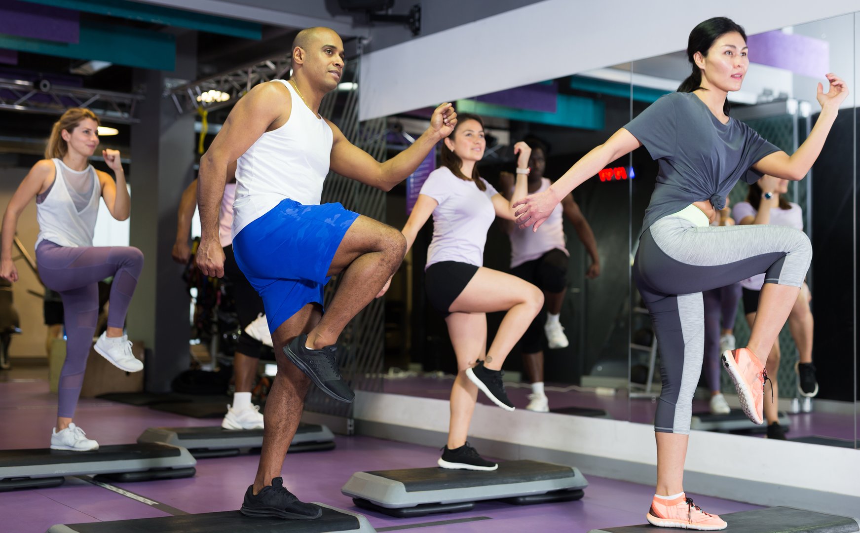 Group of sporty people working out with steppers in fitness center