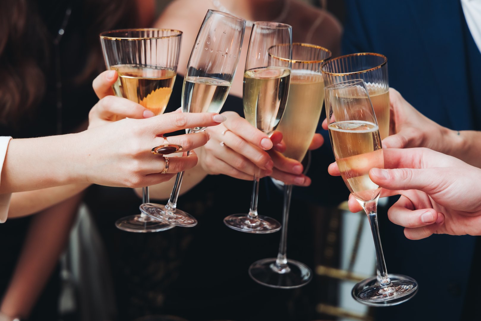 Group of guests celebrate and raise glasses, toasting and cheering with alcohol glasses with wine and champagne in the restaurant on corporate christmas birthday party event or wedding celebration