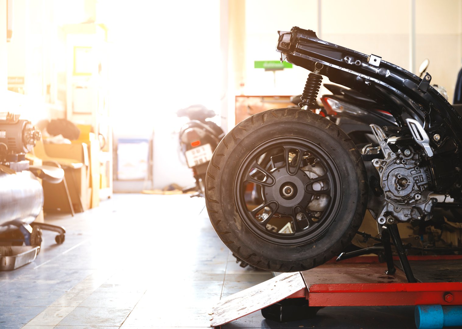 detailed shot of a motorcycle wheel on a red lift inside a garage workshop, surrounded by tools and equipment in the background.