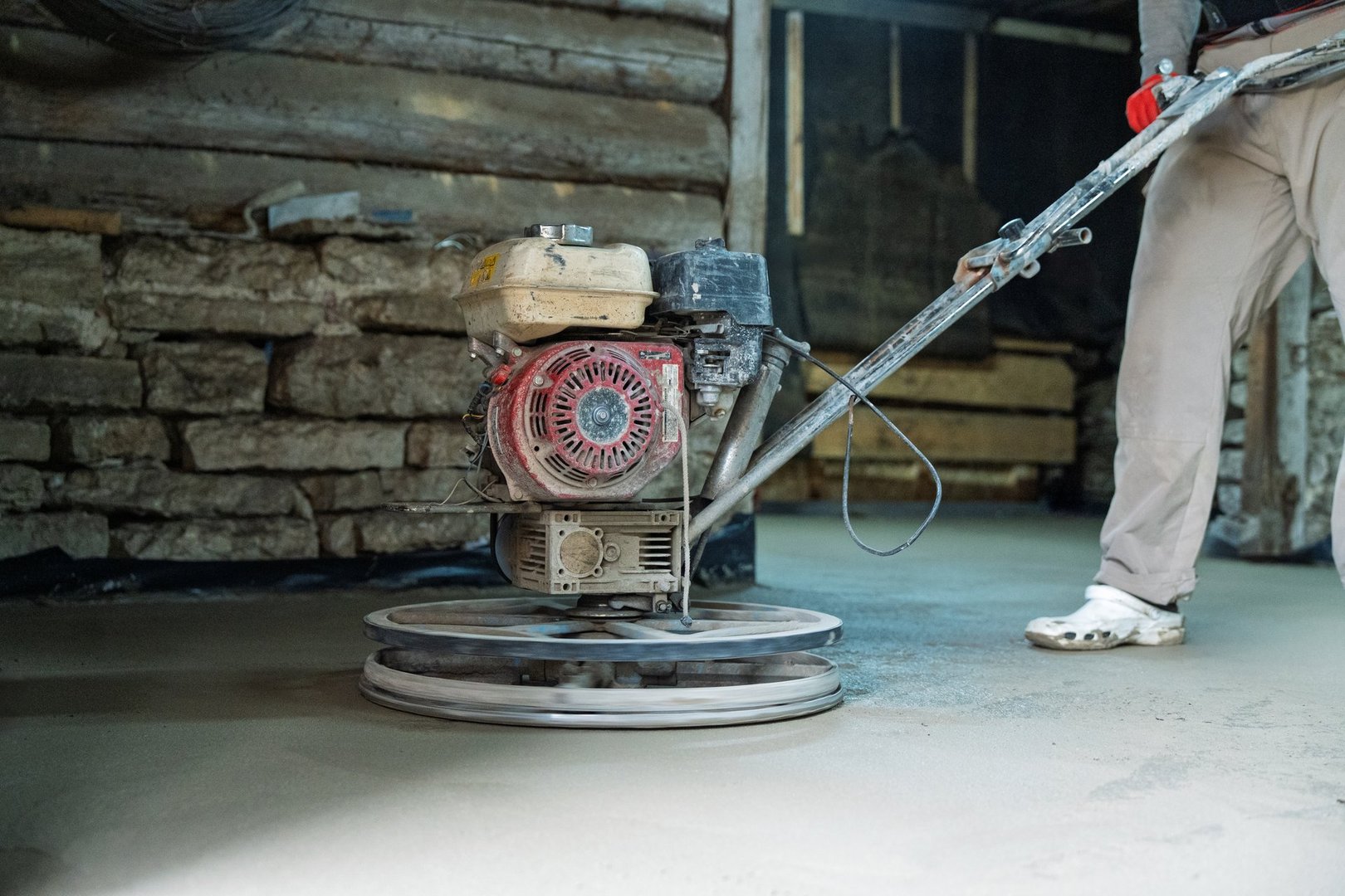 A construction worker operates a power trowel to smooth and finish a concrete surface.