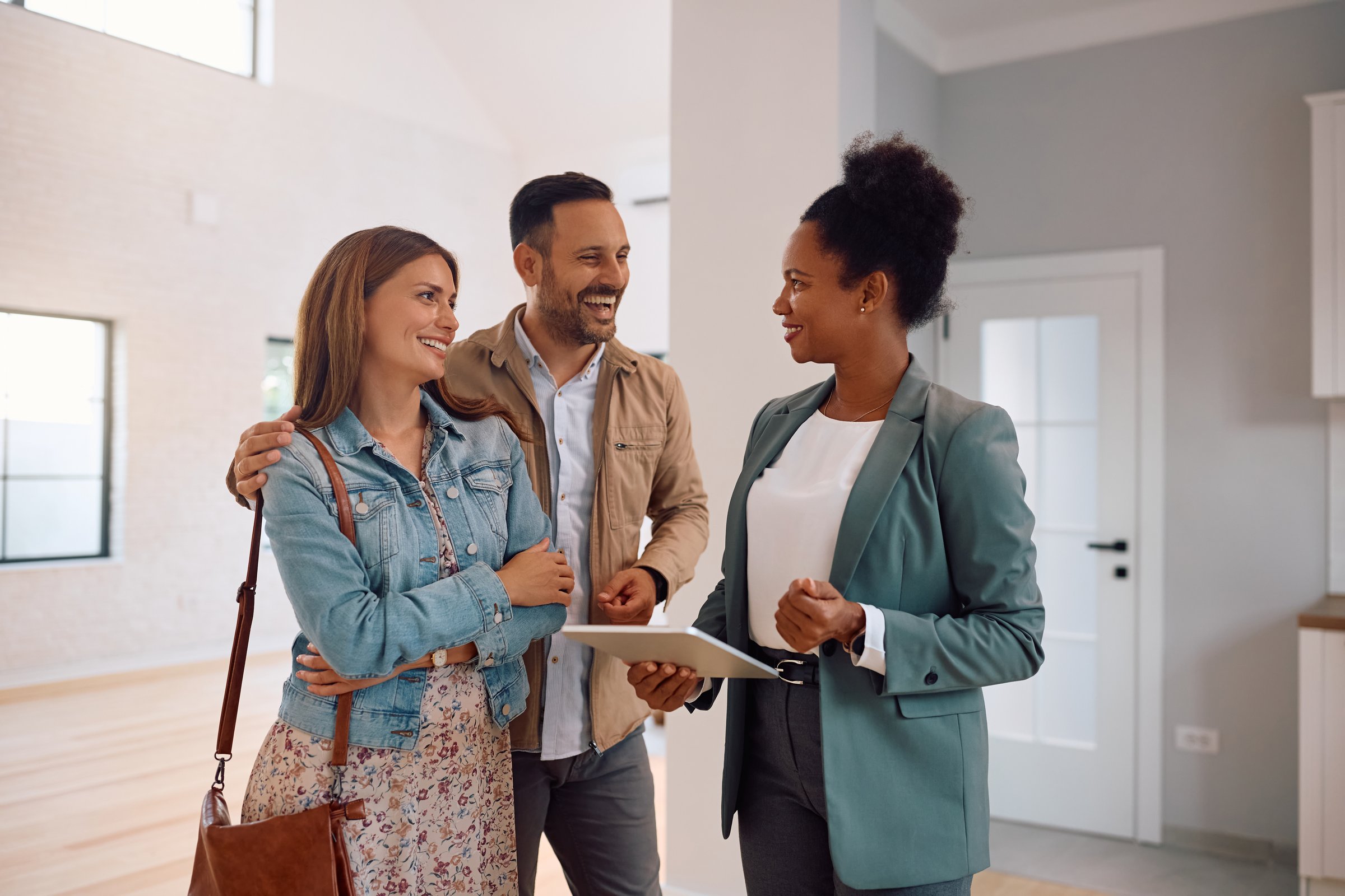 African American real estate agent using touchpad while talking to happy couple who is buying new house.
