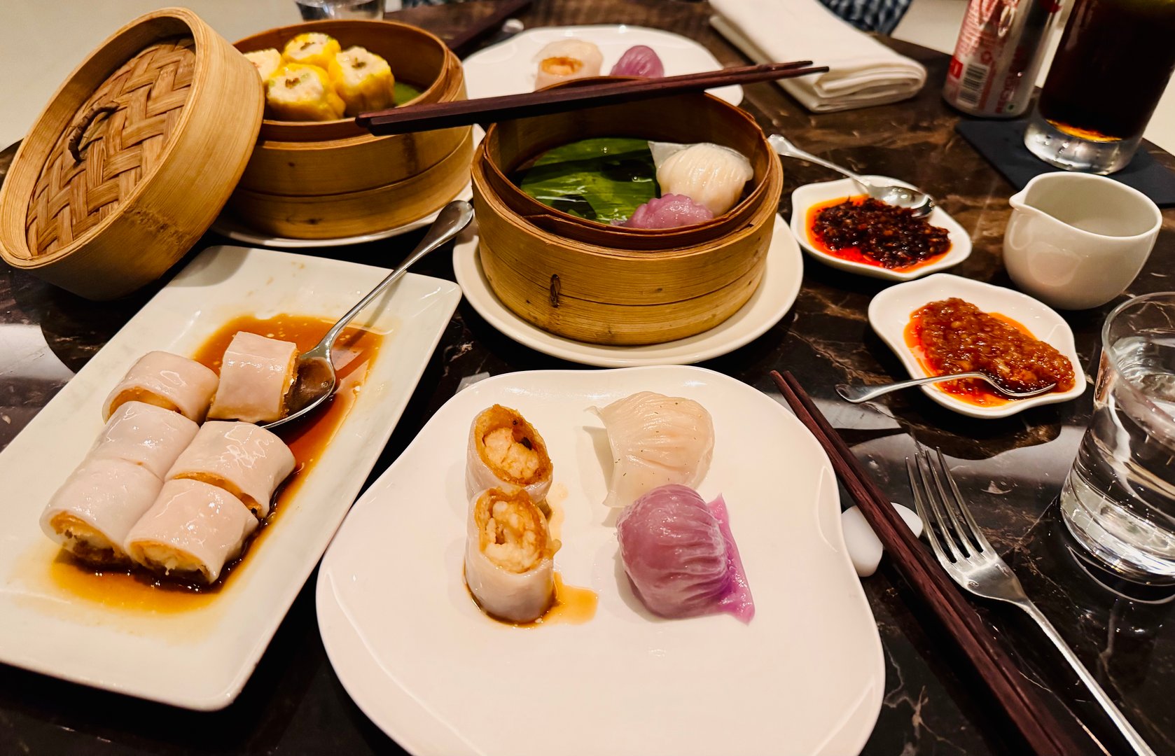 A beautifully arranged dim sum meal is presented on a dark marble table, featuring a variety of traditional Chinese delicacies served in bamboo steamers and on ceramic plates.