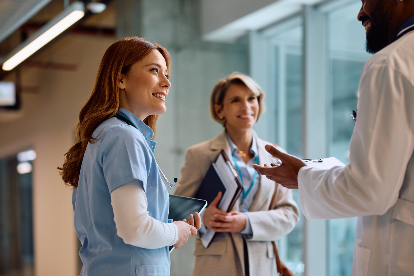Happy nurse and African American doctor talking to a businesswoman in hallway of a medical clinic.