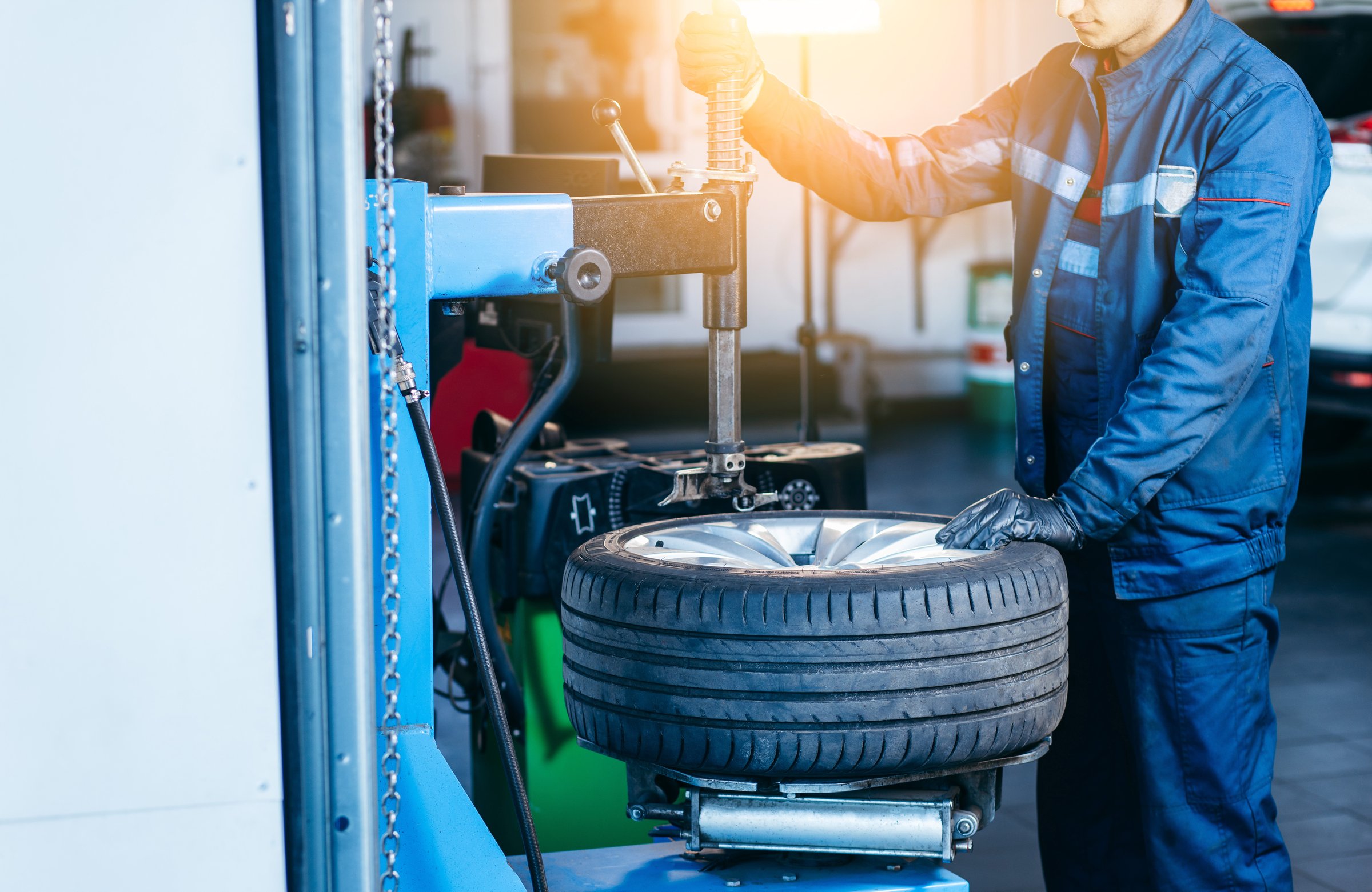 Auto mechanic loading automobile car wheel at tyre fitting machine during tire replacing auto service