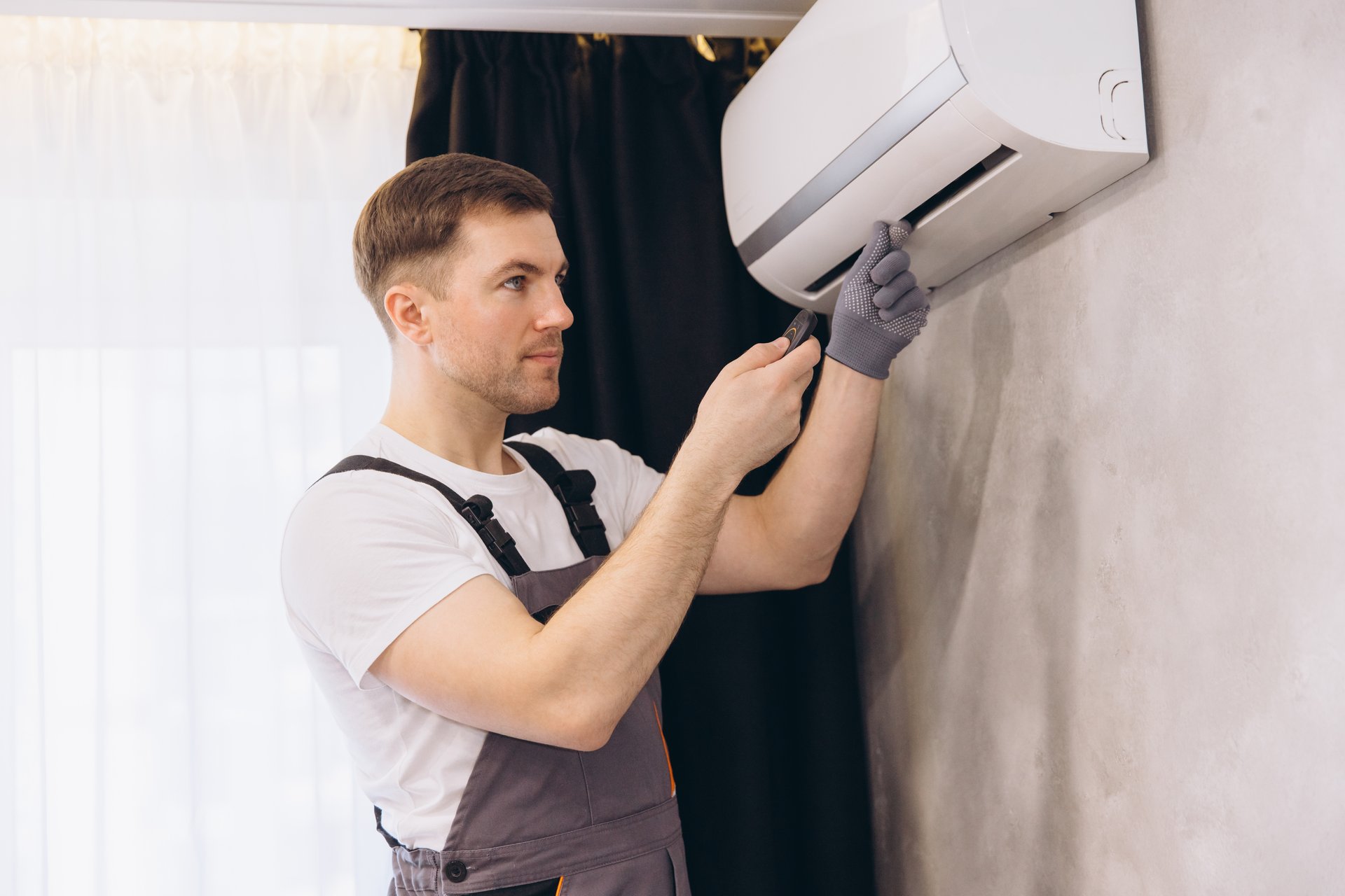 Plumber in gray uniform repairing an air conditioning unit with a screwdriver, ensuring optimal performance and comfort in the home