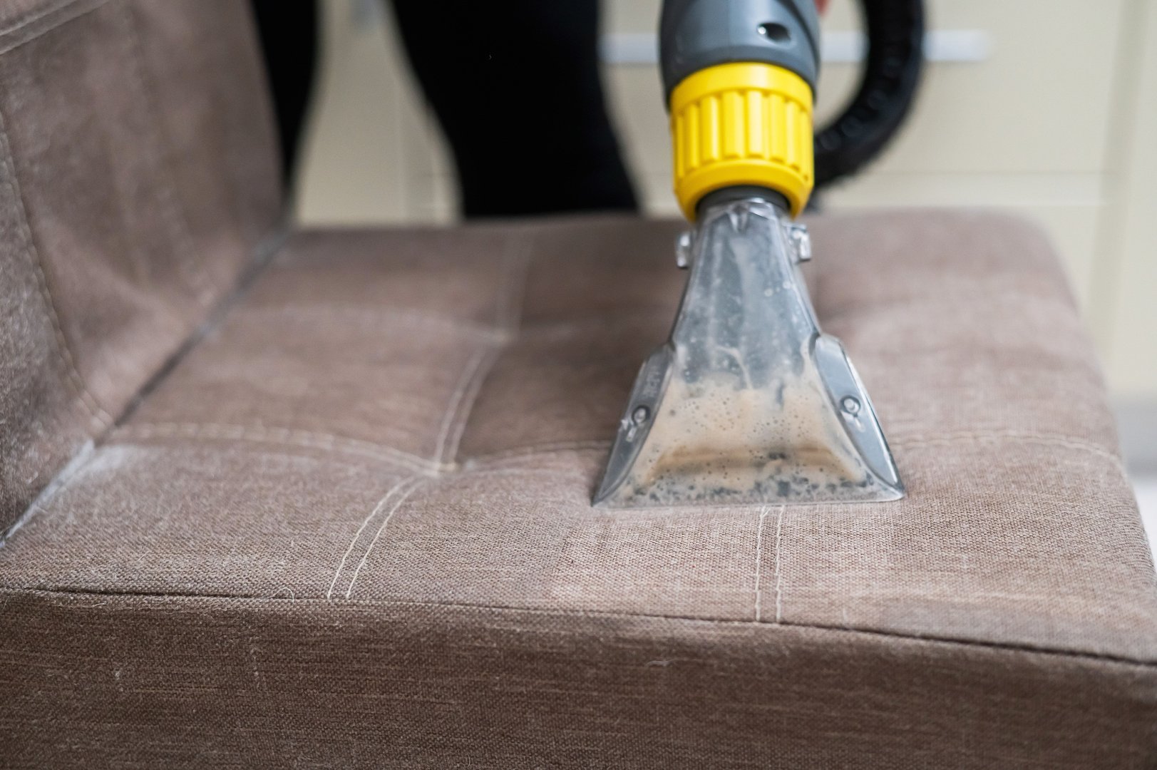 Woman cleaning a fabric chair with a professional washing vacuum cleaner