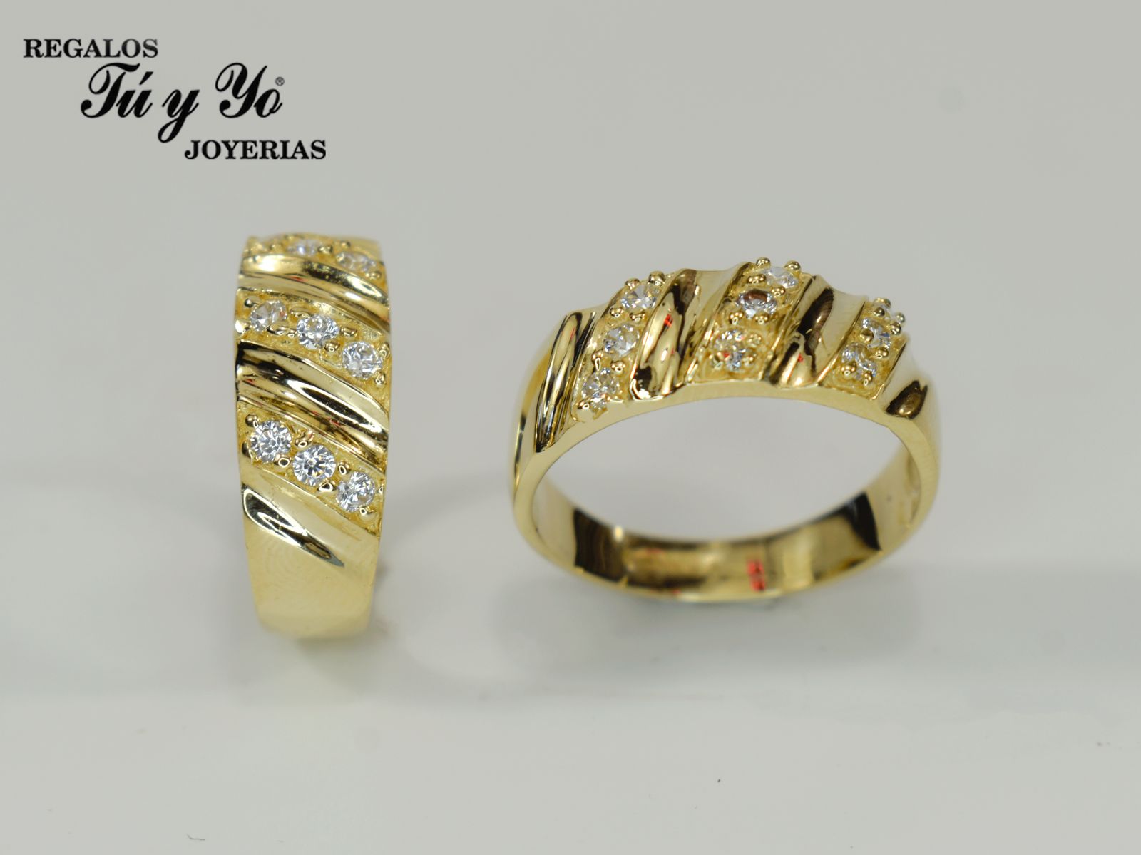 Two gold rings with diagonal diamond accents, displayed on a white background. Branding text in the top left corner.