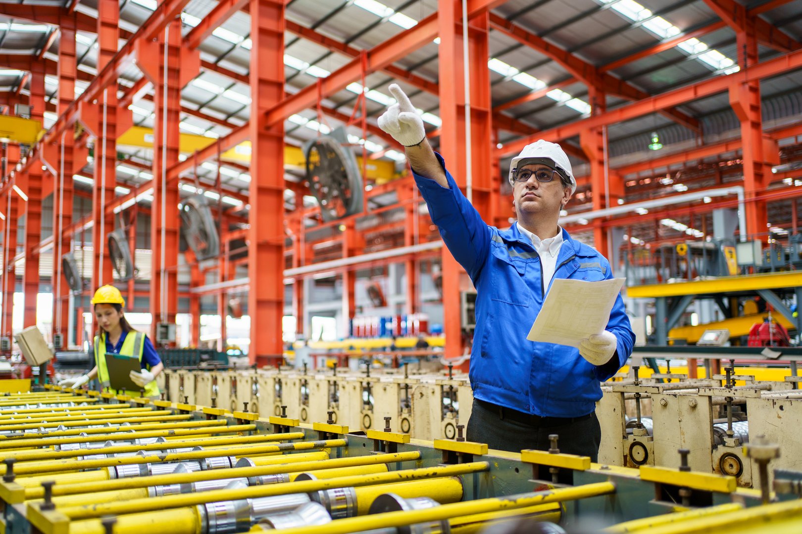 Factory technician and mechanical engineer inspecting machinery maintenance schedule together, female technician holding a detailed equipment report while analyzing industrial repair workflow.