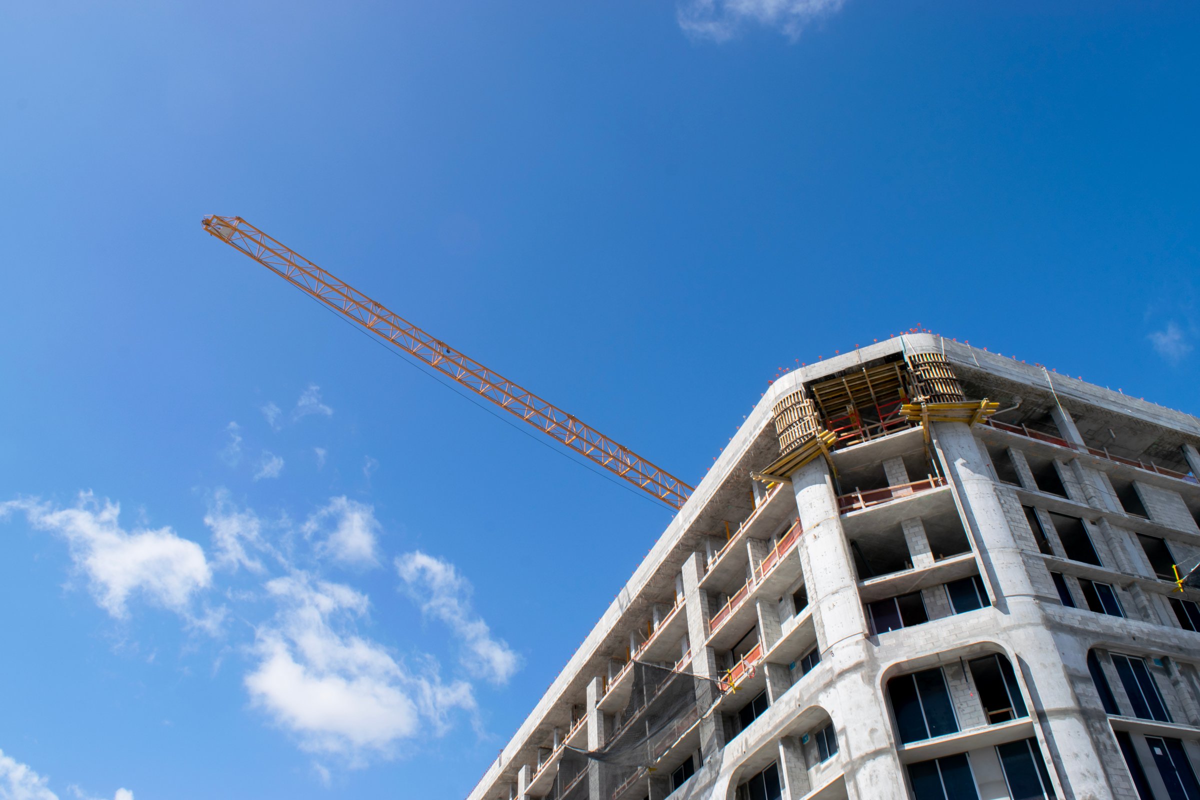 View of a construction site featuring a yellow crane and the framework of a multi-story building under construction blue sky background