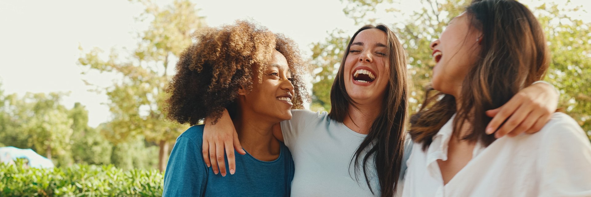 Happy multiethnic young womens talking while sitting on park bench on summer day outdoors, Panorama. Group of girls talking and laughing merrily in city park