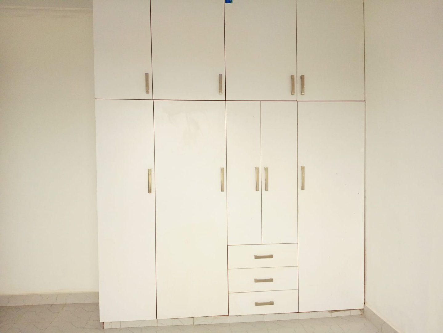 White built-in wardrobe with multiple cabinets and drawers, featuring silver handles, set against a plain wall.