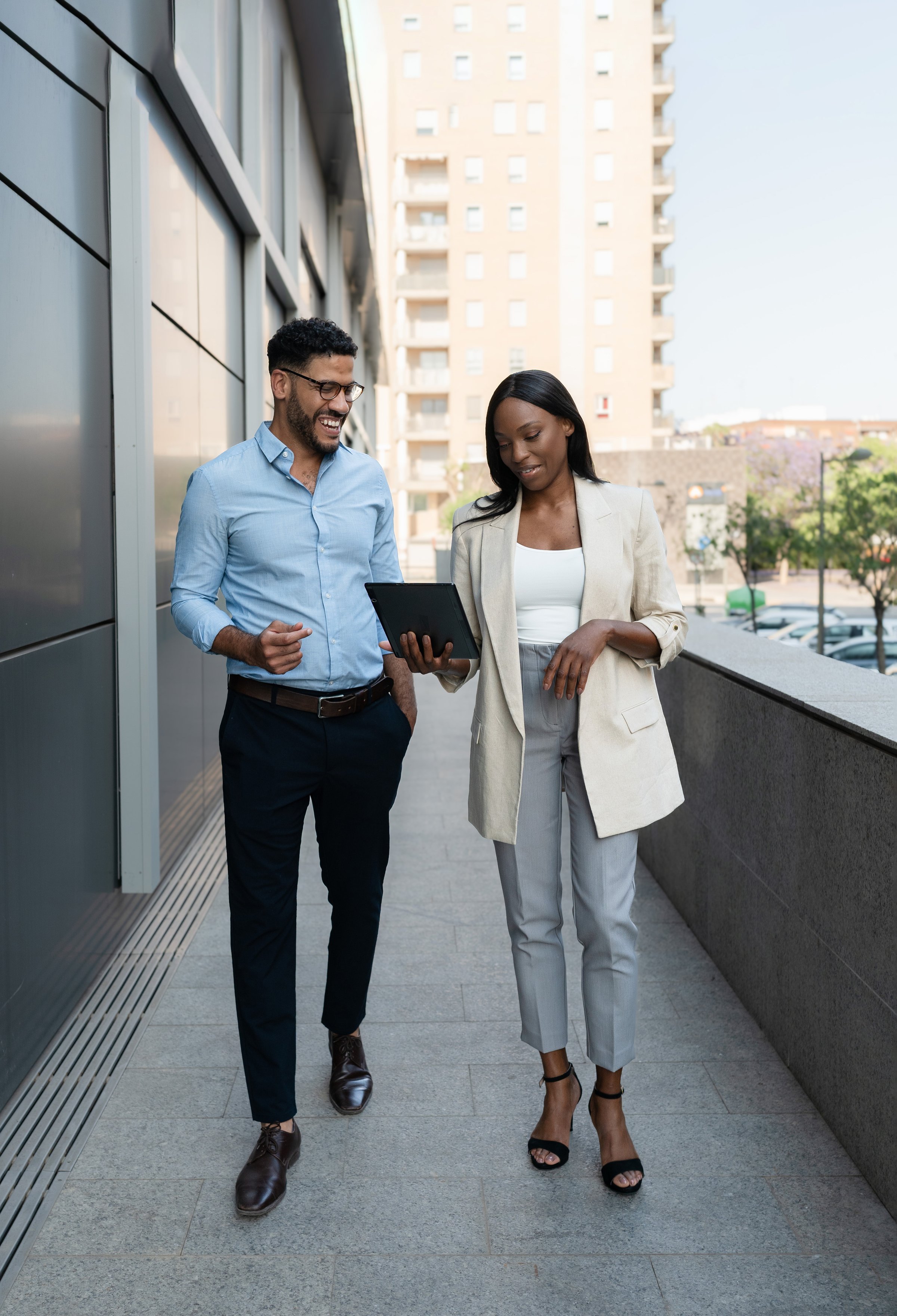 Smiling Two Multiracial business partners walking outside office building using tablet