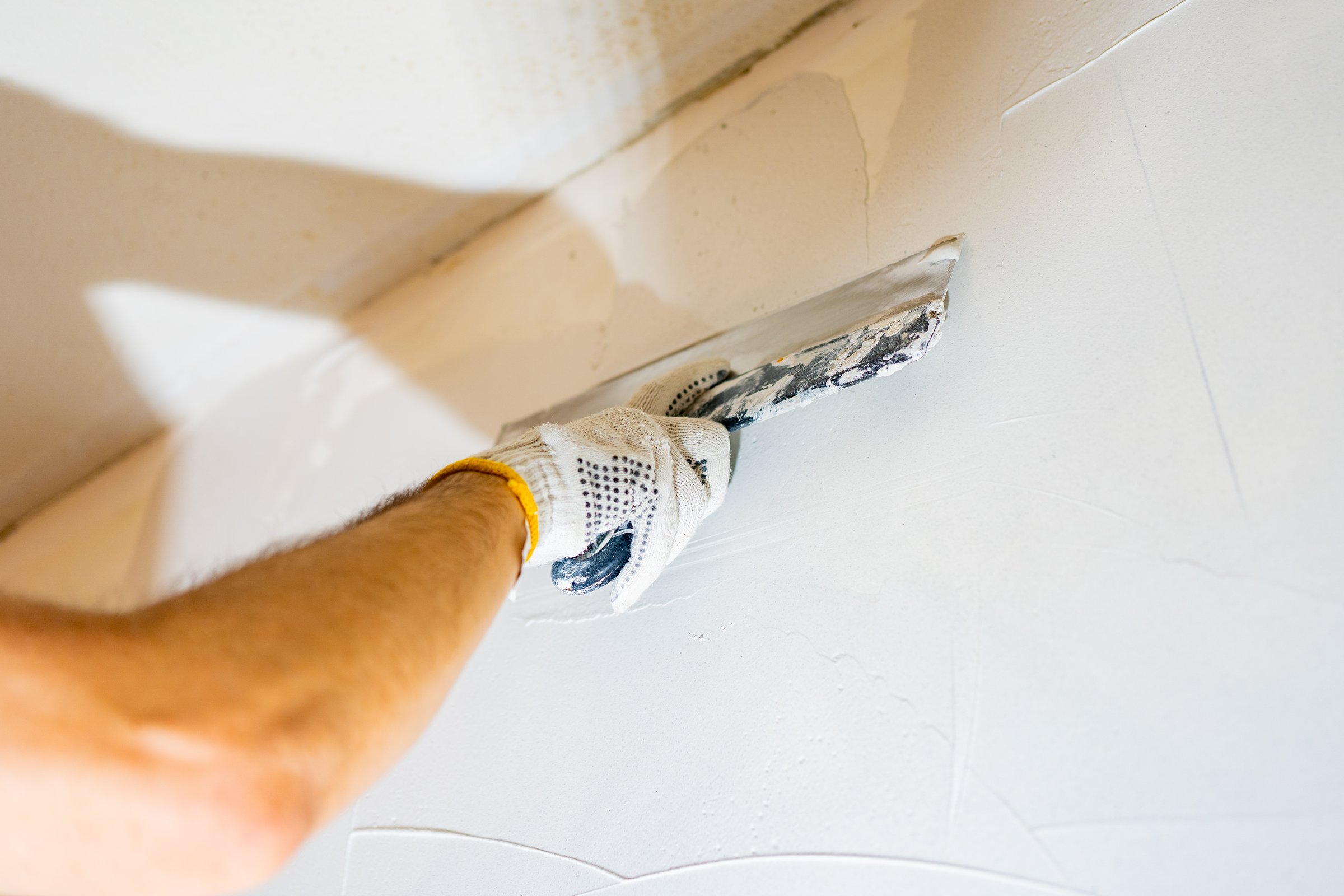 Wall preparation in progress; a worker meticulously smooths drywall mud onto the surface, ensuring a flawless base for paint.