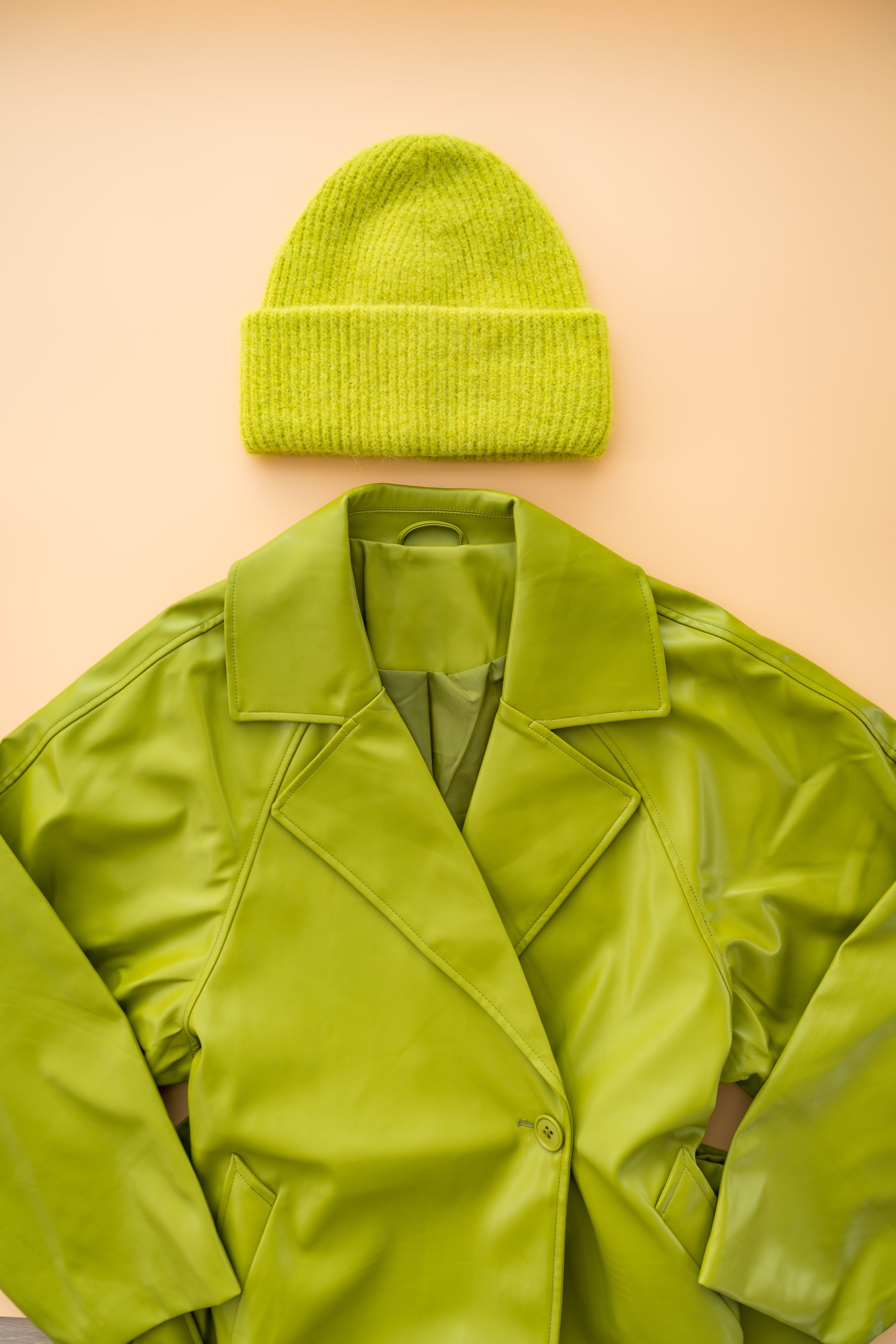 Flat lay photograph of a vibrant trend green faux leather coat and soft cashmere hat, crafted from recycled materials. Captured with natural light, top-down perspective, and ample copy space