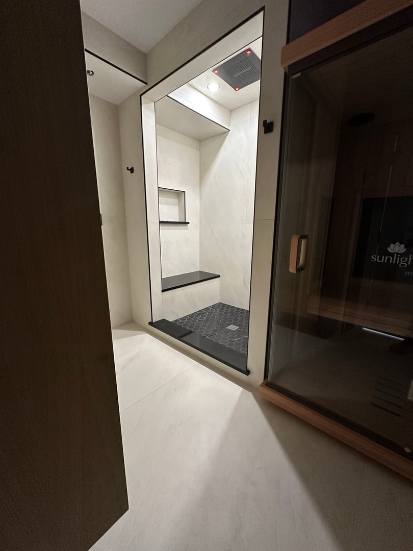 Modern bathroom with a large glass-enclosed shower and adjacent sauna door, featuring sleek minimalist design.