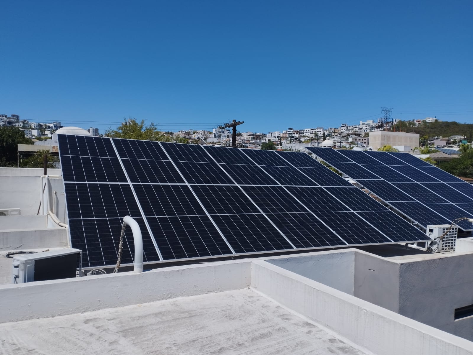Solar panels on a rooftop with a clear sky and distant view of a residential area in the background.