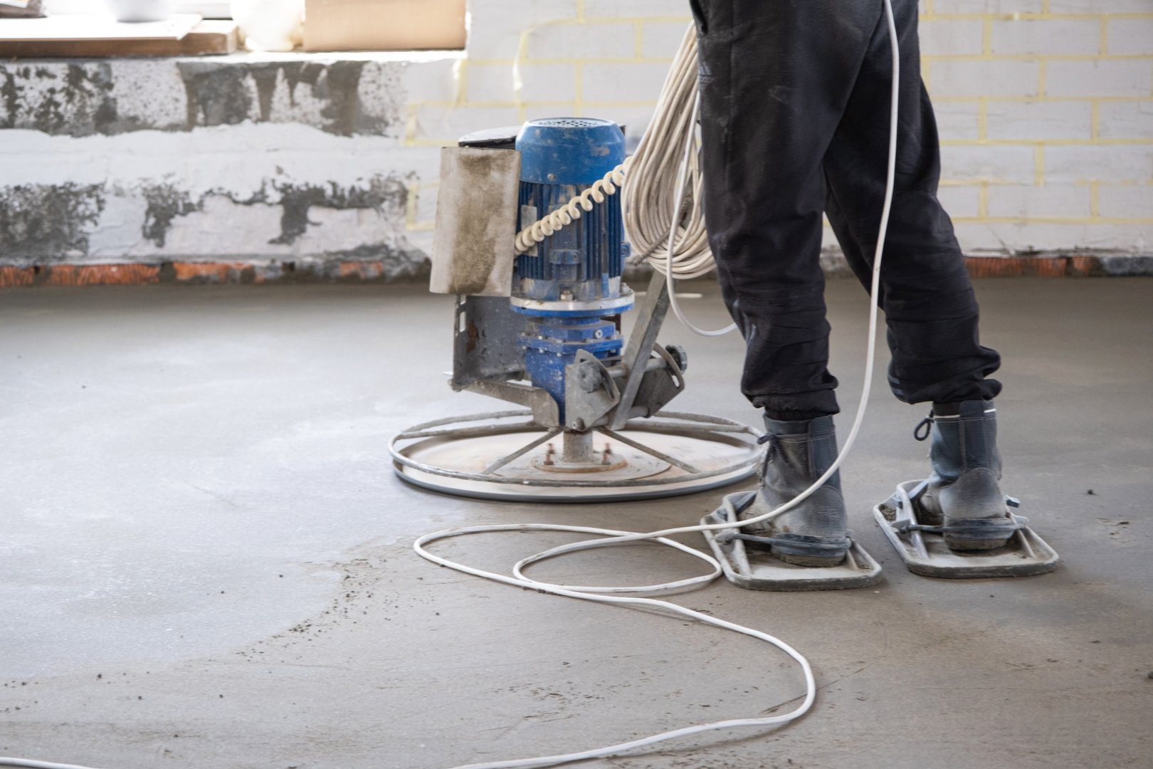 Yarı kuru zemin şapının döner diskli makine ile sıkıştırılması ve taşlanması işlemi. Evde beton zemin inşaatı, özel ekipmanla çalışan usta.