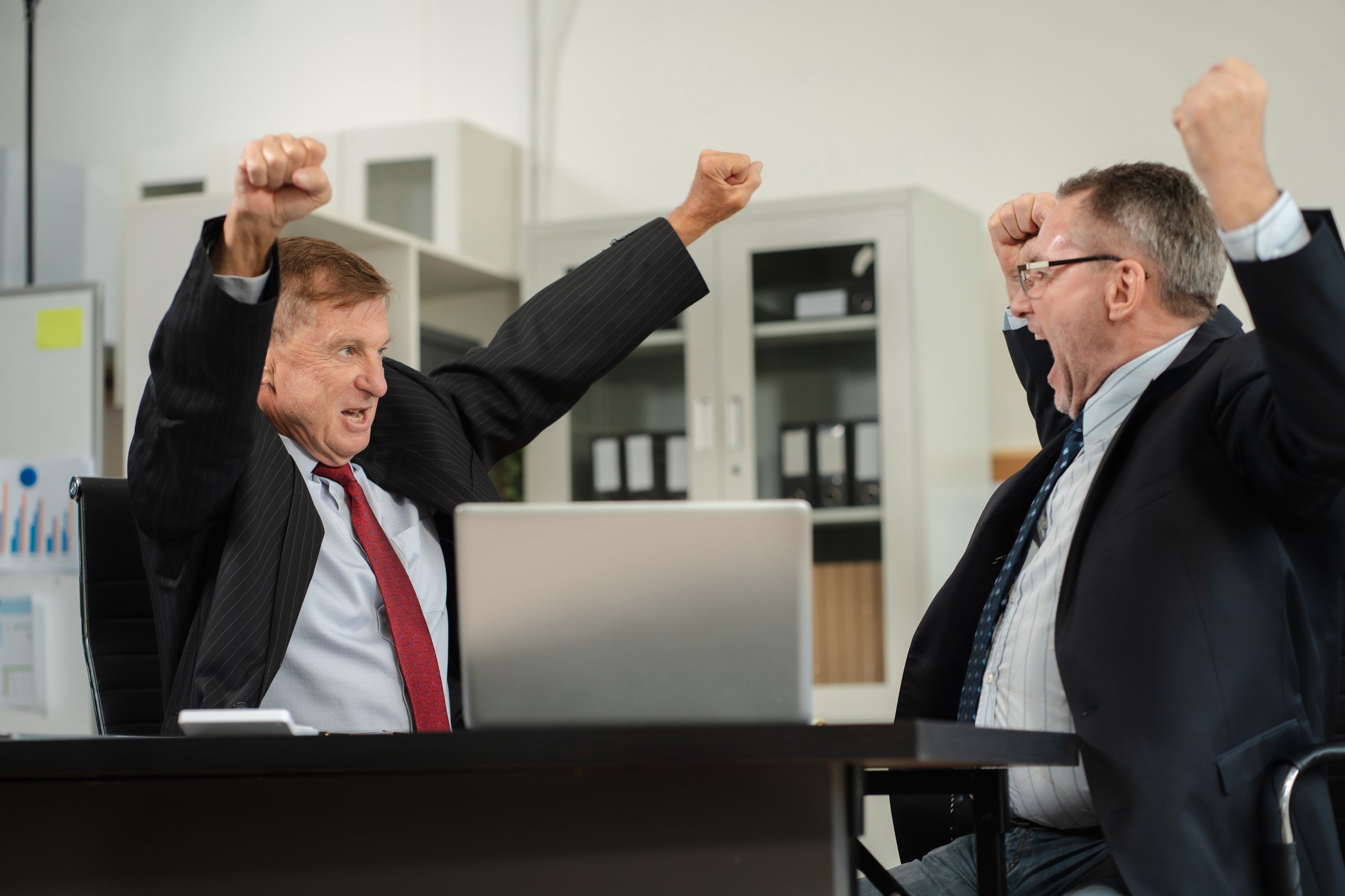 Successful business team, excited mature businessman Keeping up arms and showing positive emotions, happy working in modern office on computer.