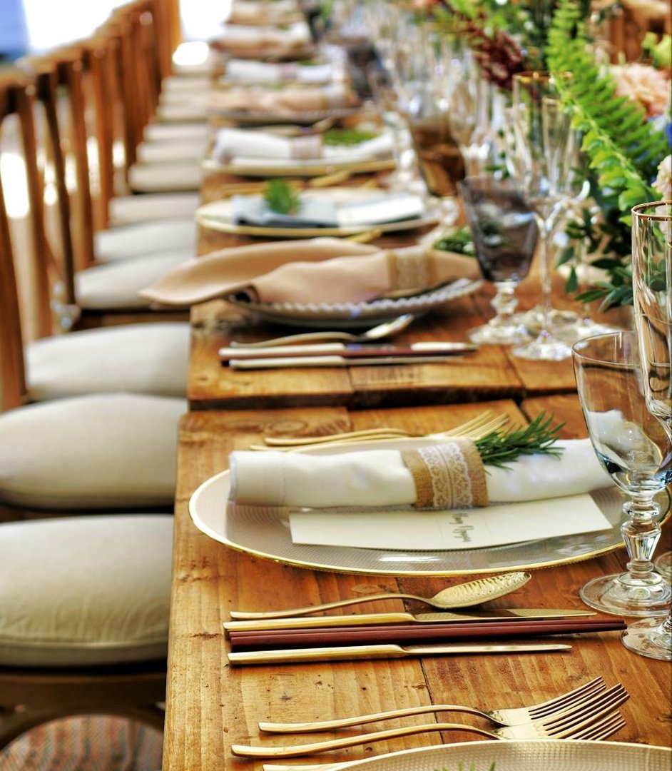 Elegant table setting with gold cutlery, crystal glasses, and napkin-wrapped plates on a wooden surface.