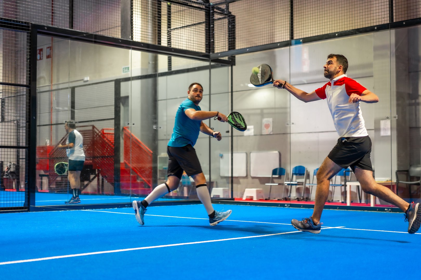 Mature caucasian male friends playing paddle tennis energetically in a blue indoor court