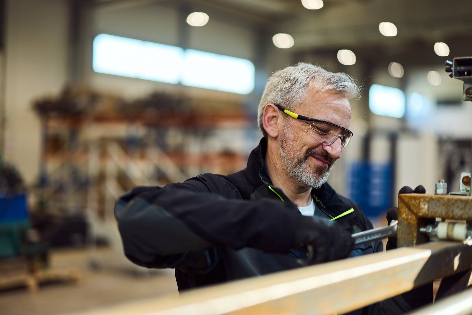 Mature worker in safety gear using tools in an industrial workshop setting.