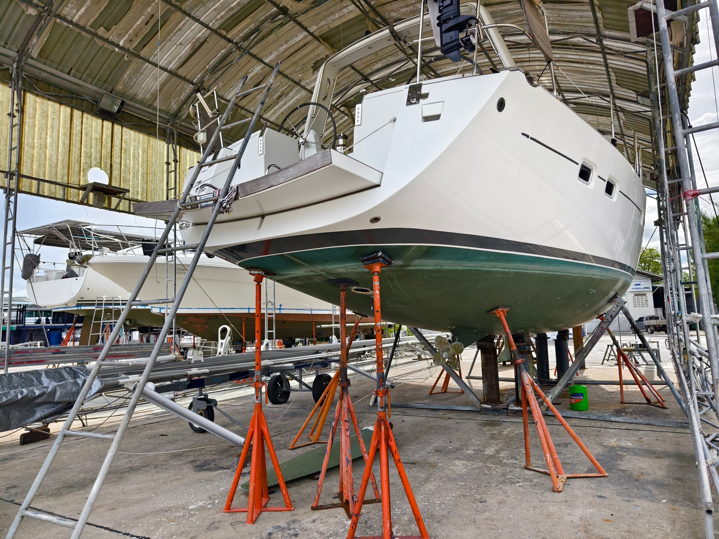 A boat is carefully lifted under a covered structure for essential maintenance, showcasing preparations and tools
