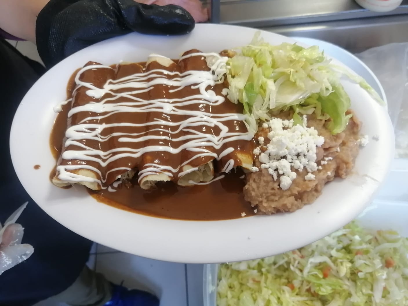 Plate of enchiladas topped with sauce and sour cream, served with refried beans, cheese, and lettuce.