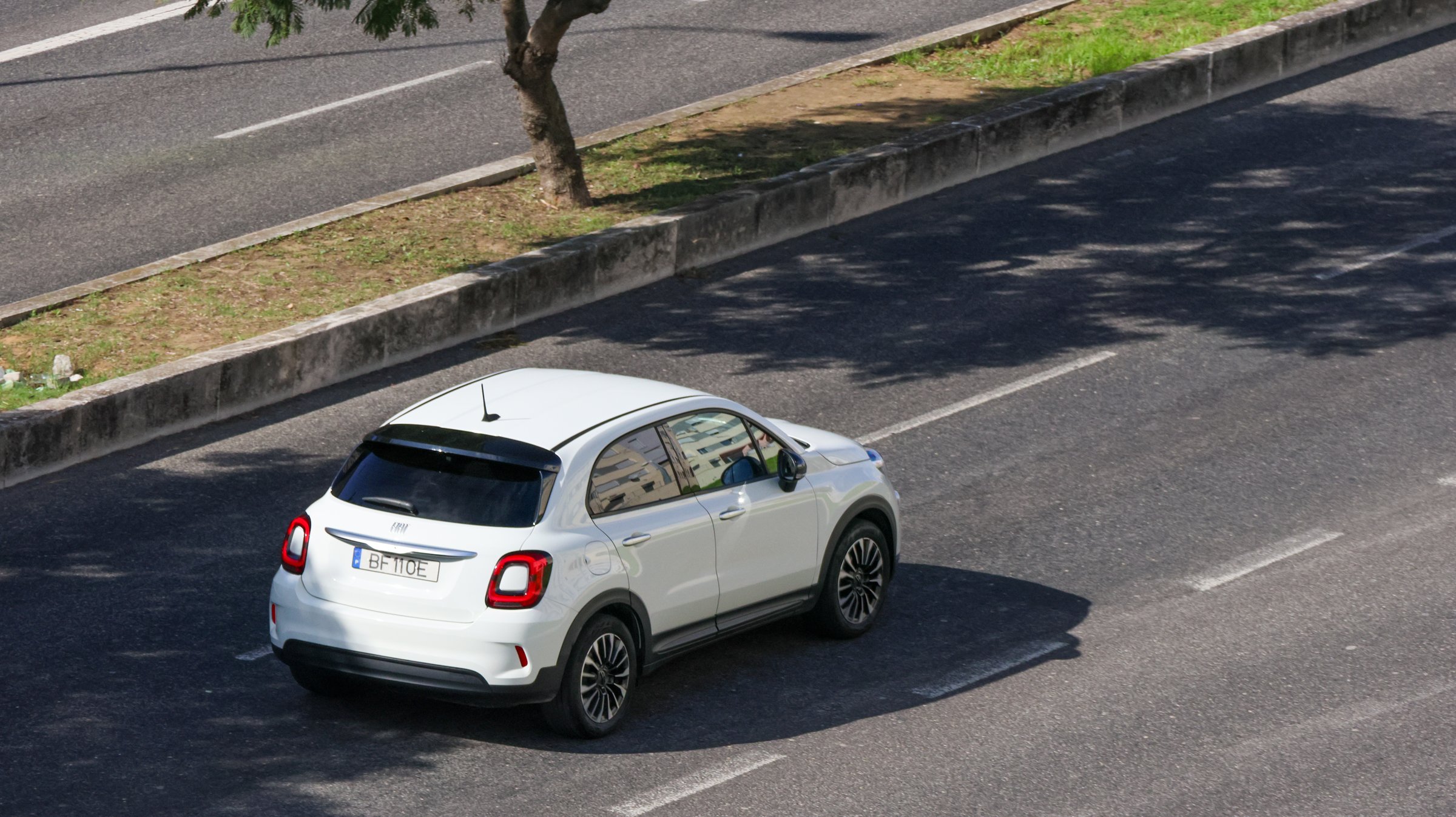 Lisbon, Portugal, October 31, 2024, Modern white fiat 500x car driving on asphalt road near a tree in a sunny day