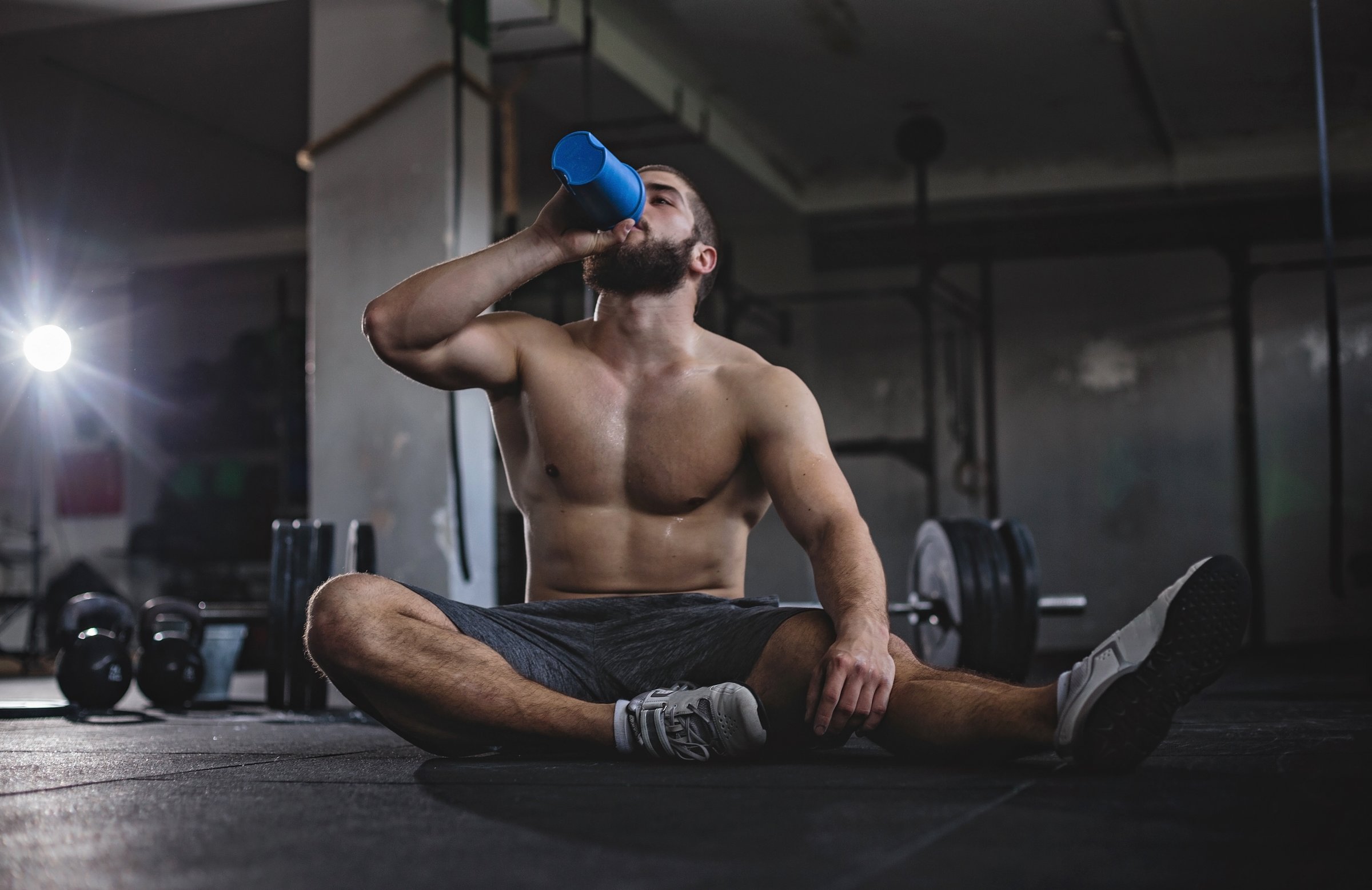 Young body builder sitting on the floor in the gym and drinking water