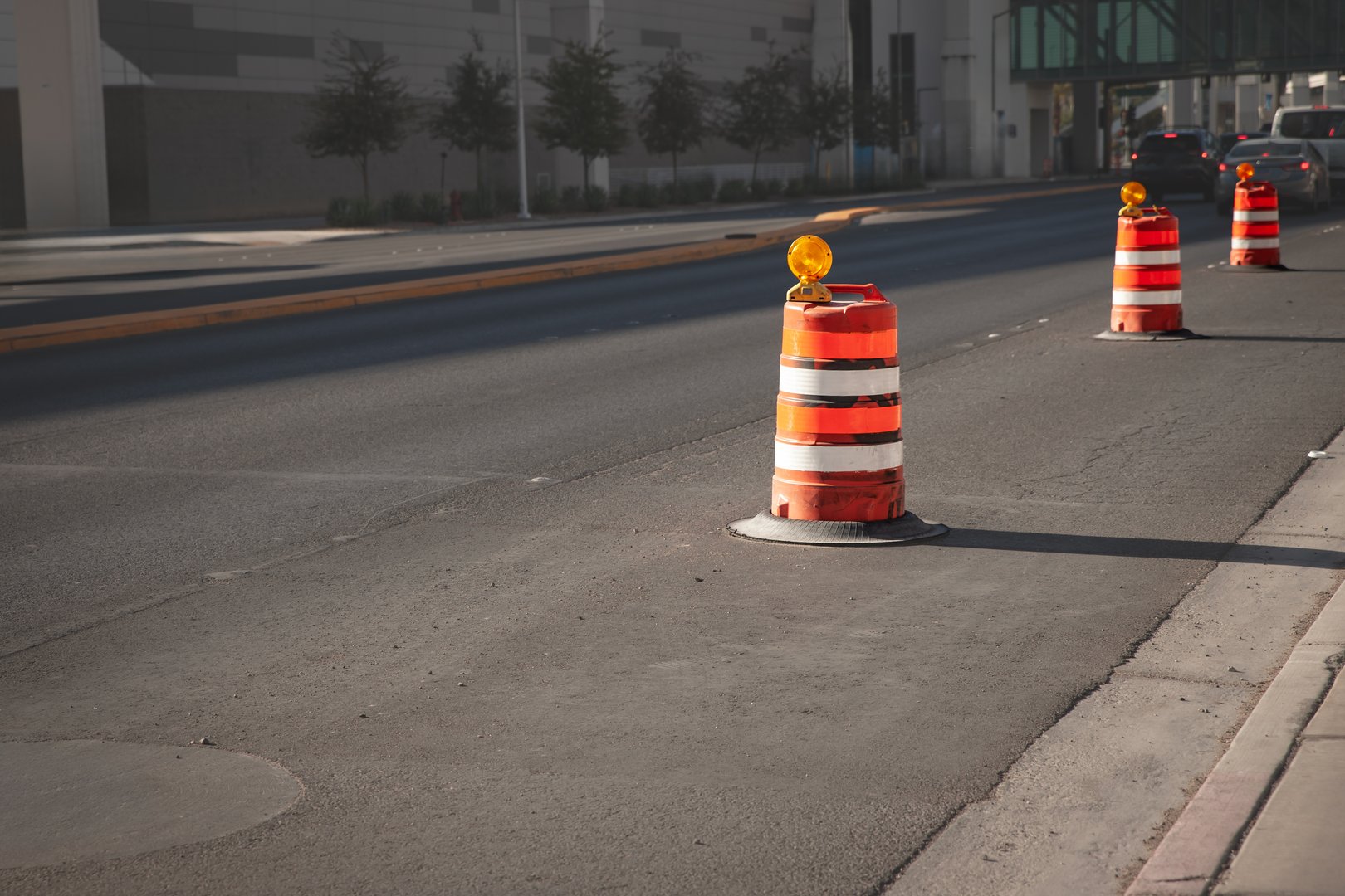 This photograph captures a row of bright orange construction barrels positioned along a roadway in Las Vegas. Commonly used for traffic control, these barrels indicate an active road work zone where renovations or repairs are underway. The vivid color and repetitive pattern of the barrels draw immediate attention, highlighting safety measures taken during infrastructure projects. The urban setting underscores the continuous development and maintenance required in bustling cities across the USA. The image reflects on themes of urban growth, the complexities of traffic management, and the essential nature of such equipment in ensuring both worker and commuter safety. It also provides insight into the often-overlooked aspects of city life that keep urban environments functional and efficient.