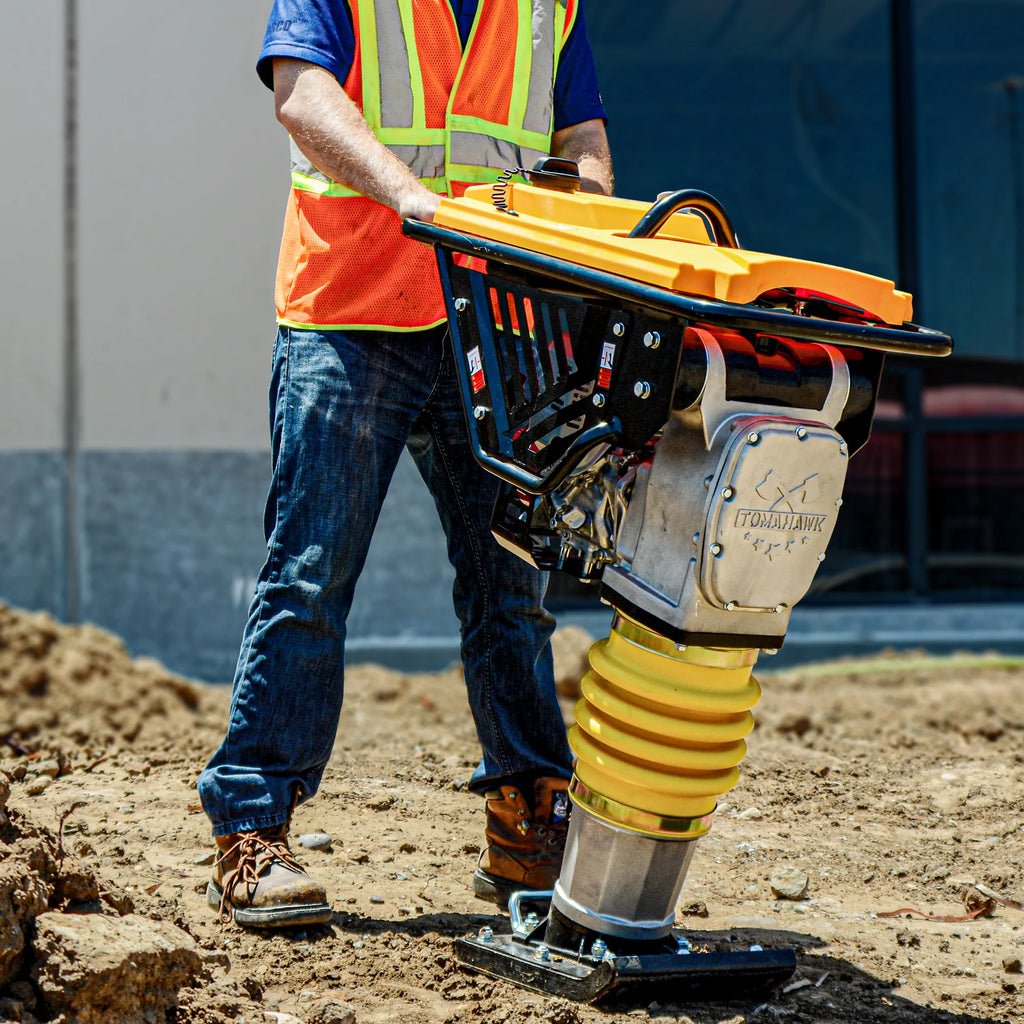 Construction worker using a yellow and silver vibratory compactor on a dirt surface outdoors.
