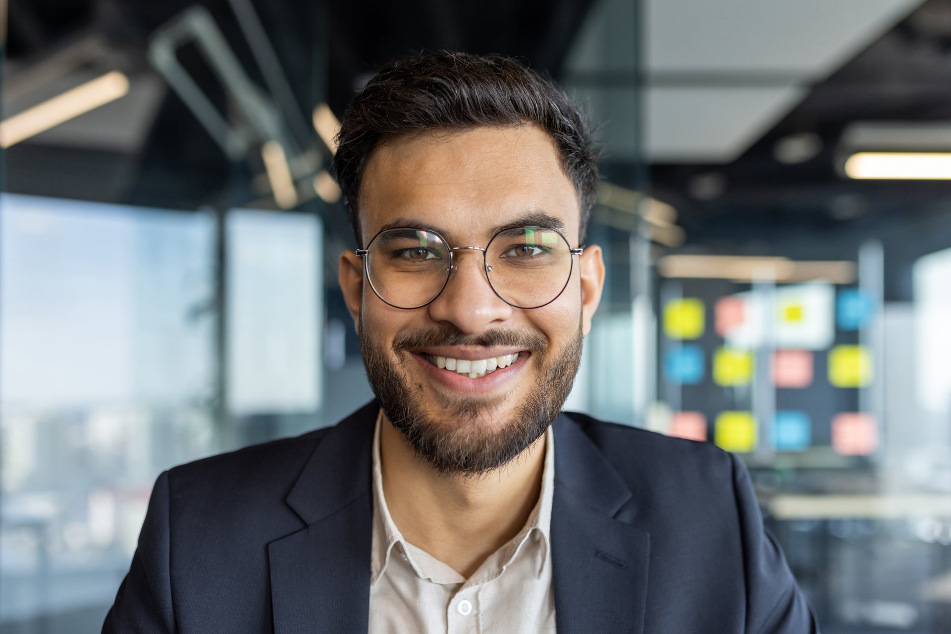 Portrait of successful young businessman at workplace inside office. Man smiling close up and looking at camera, satisfied financier investor.