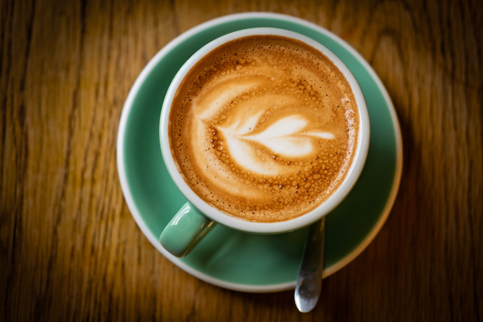 A close-up overhead shot of a latte with latte art on a wooden table.