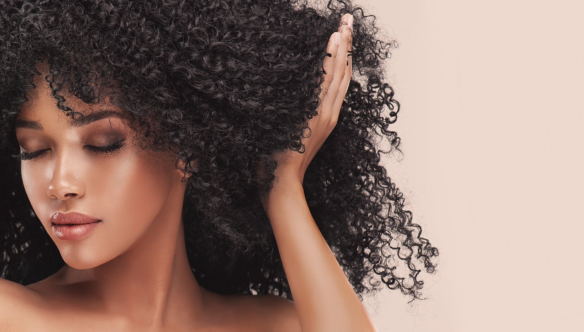 Young attractive brown skinned model is touching own dense, curly black hair in moment of movement.  Girl with vibrant melanin-rich skin tone. Hairstyle in Afro style.