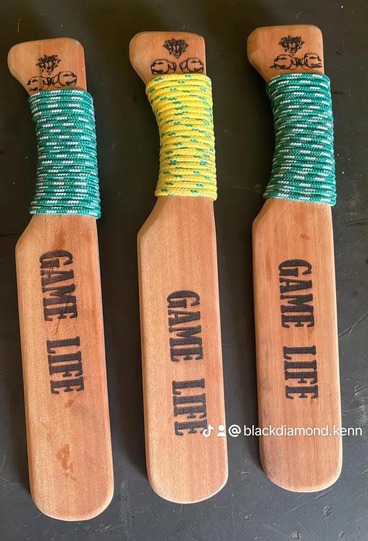 Three wooden paddles with GAME LINE printed on them, wrapped with green and yellow rope, against a dark background.
