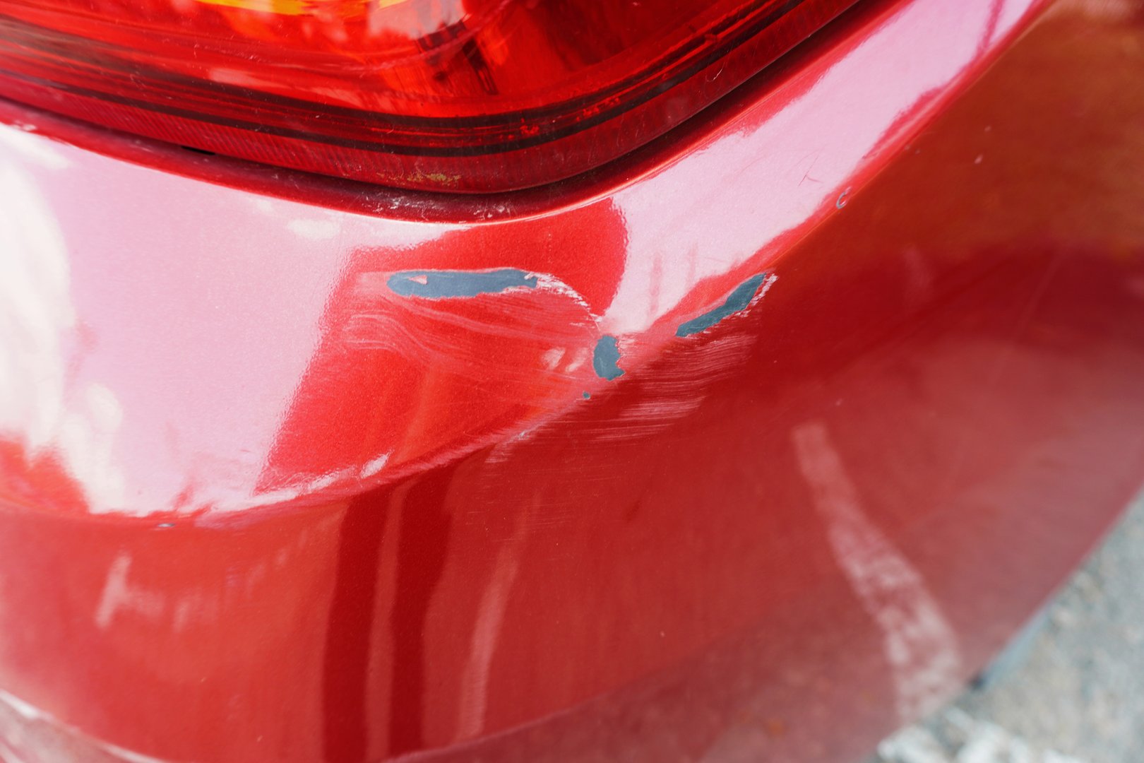 Scratch marks on the rear body of the red car. Car's rear bumper with deep scratches, paint chips, and scuff marks, exterior damage. Car accident aftermath, minor dents and scratches
