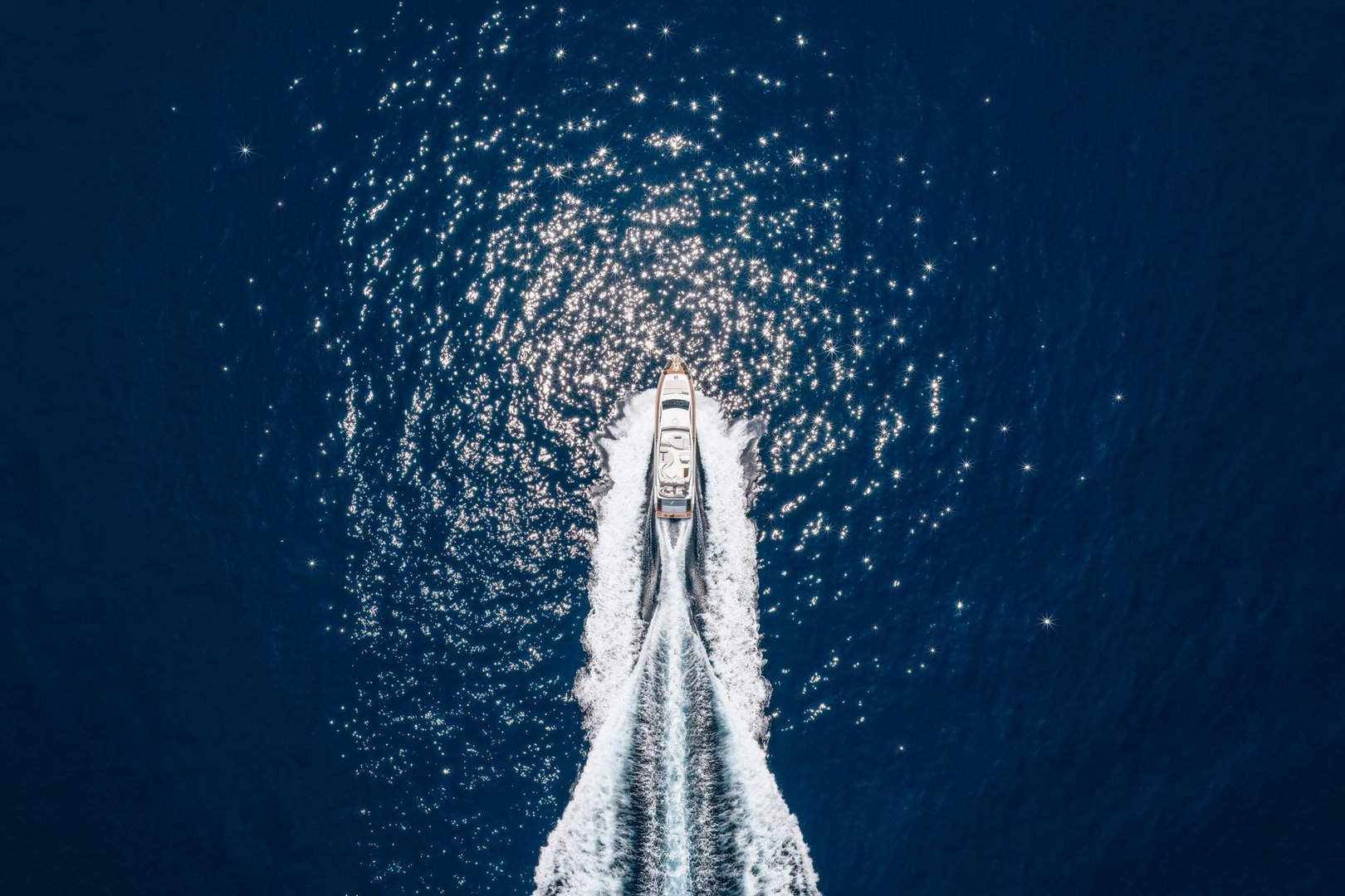 Aerial overhead view of a luxury yacht cruising with high speed over blue ocean leaving a trail of bubbles and waves behind