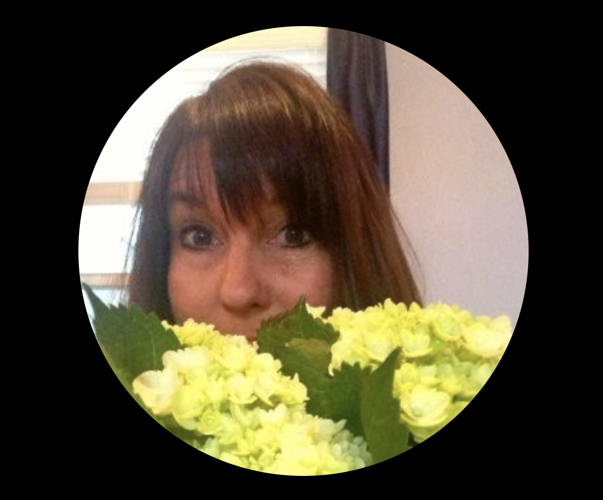 A woman with brown hair partially hidden behind a bouquet of light green hydrangeas, in a circular frame.