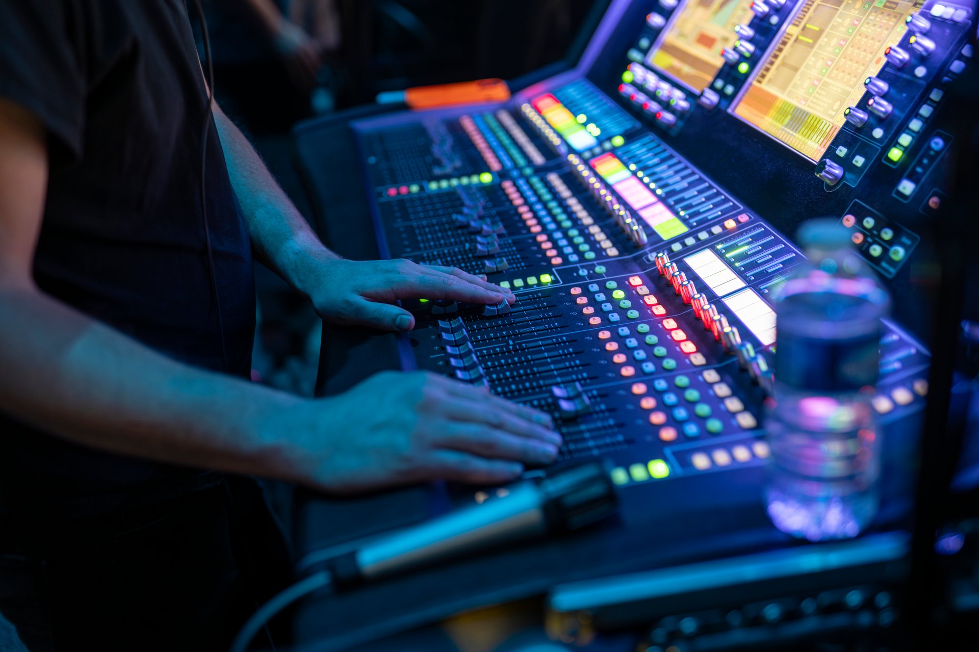 A sound technician adjusting levels on a brightly lit audio mixing console during a live event.