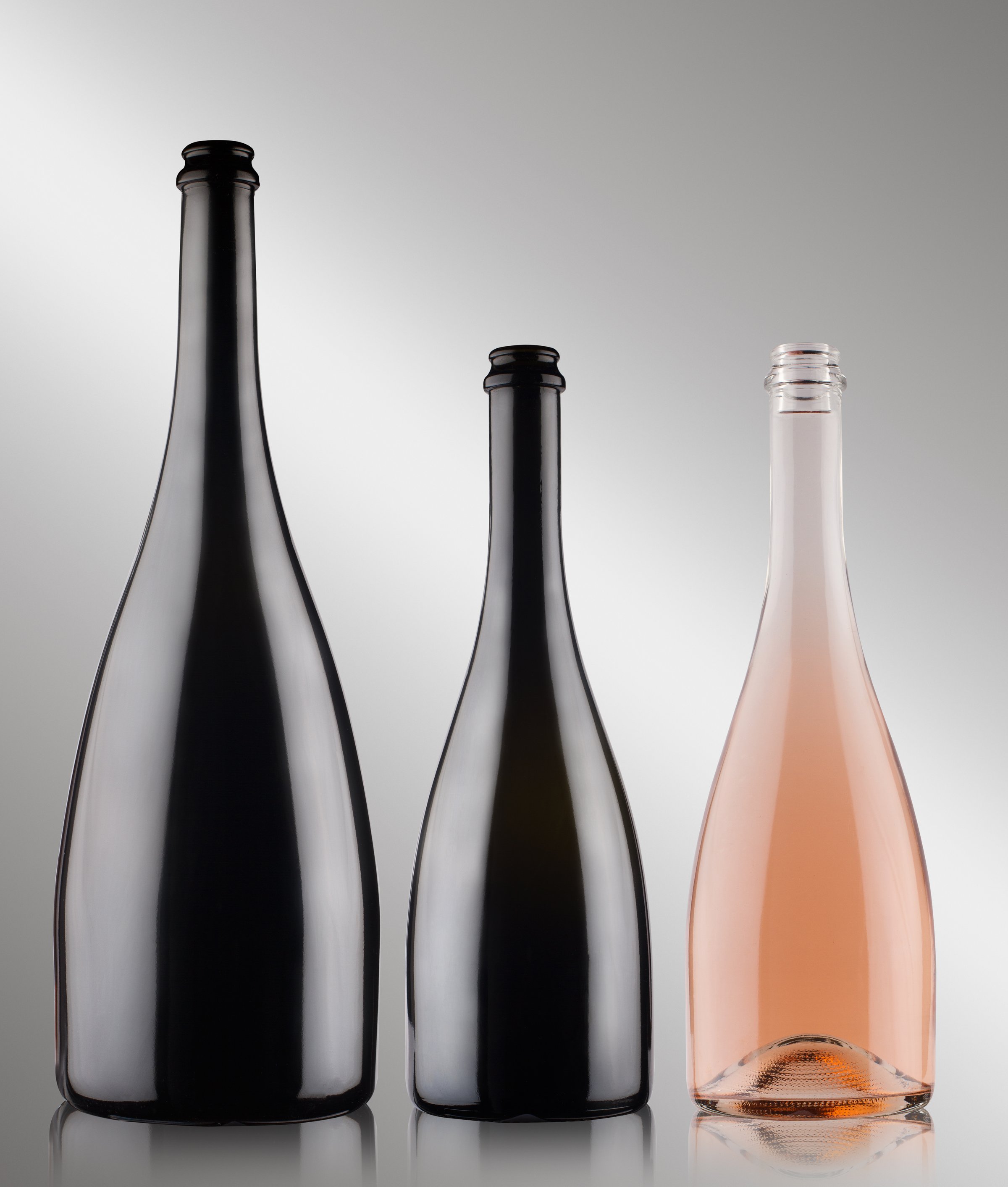 front view closeup of three champagne bottles of different sizes blank with no label two black and one rose on grey background