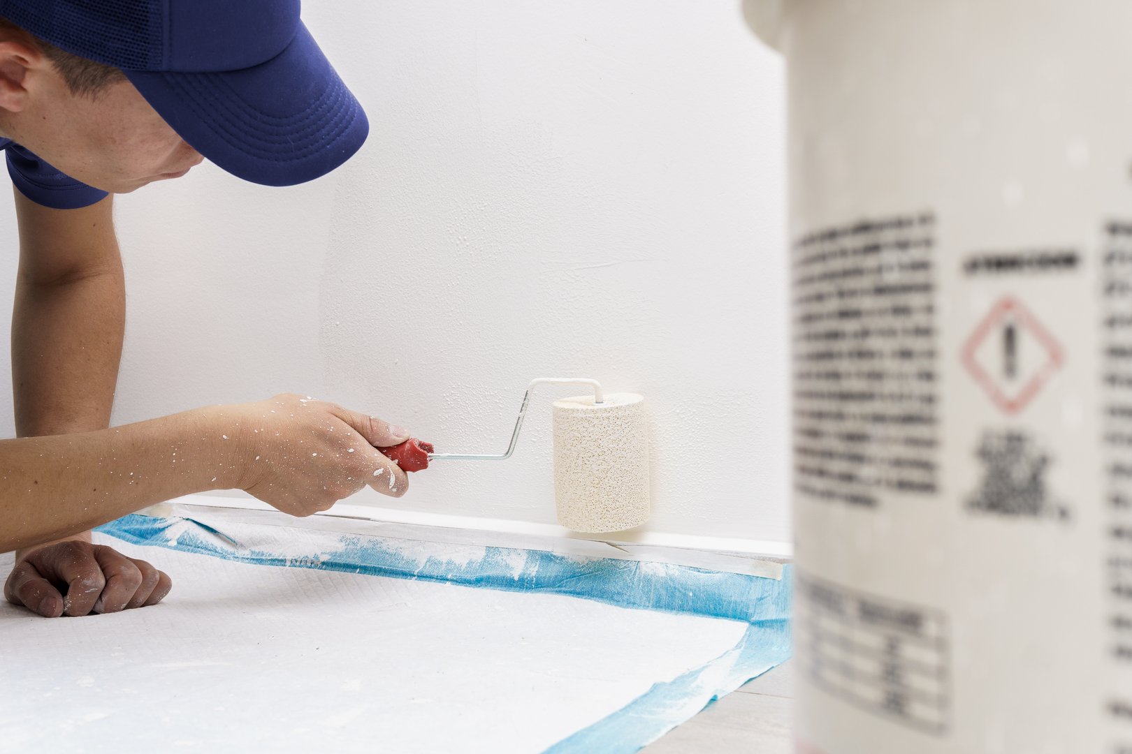 a man lying on the floor painting the wall of a house with white paint and with a roller in uniform