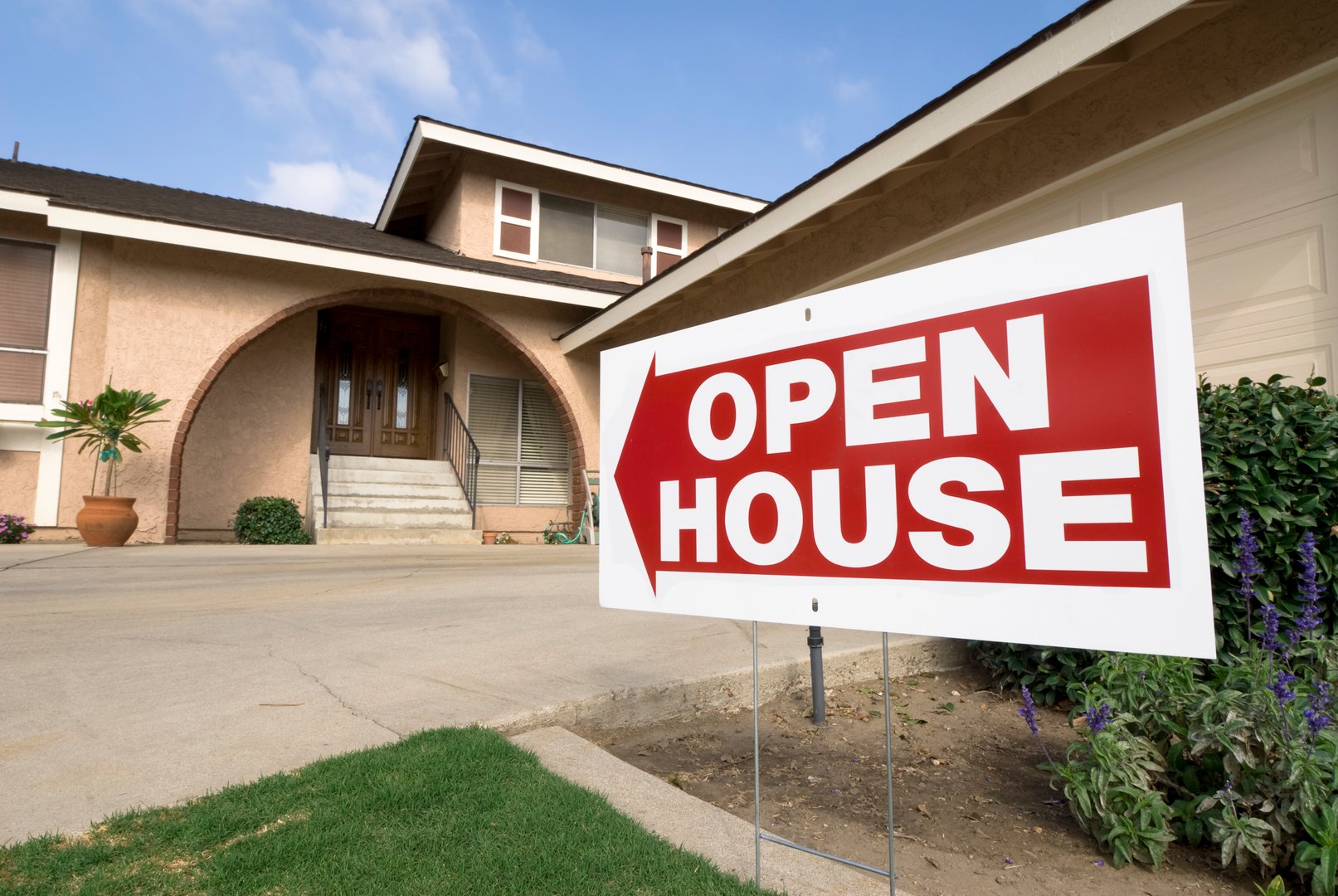 A home for sale shows the open house sign on a sunny afternoon.