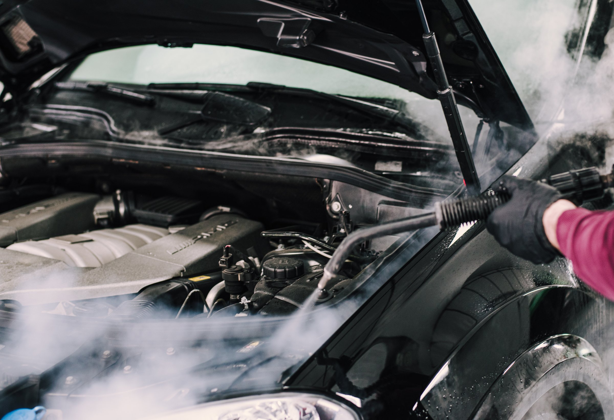 A man using steam to clean a car hood
