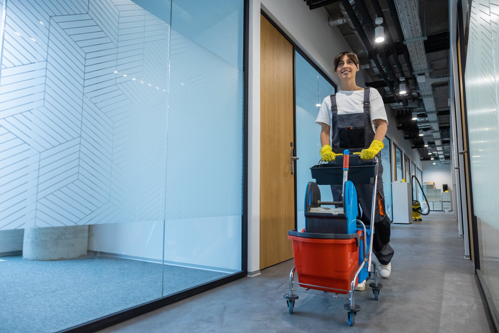 Cleaning personnel. Dark-haired young woman in uniform with a cart of cleaning equipment
