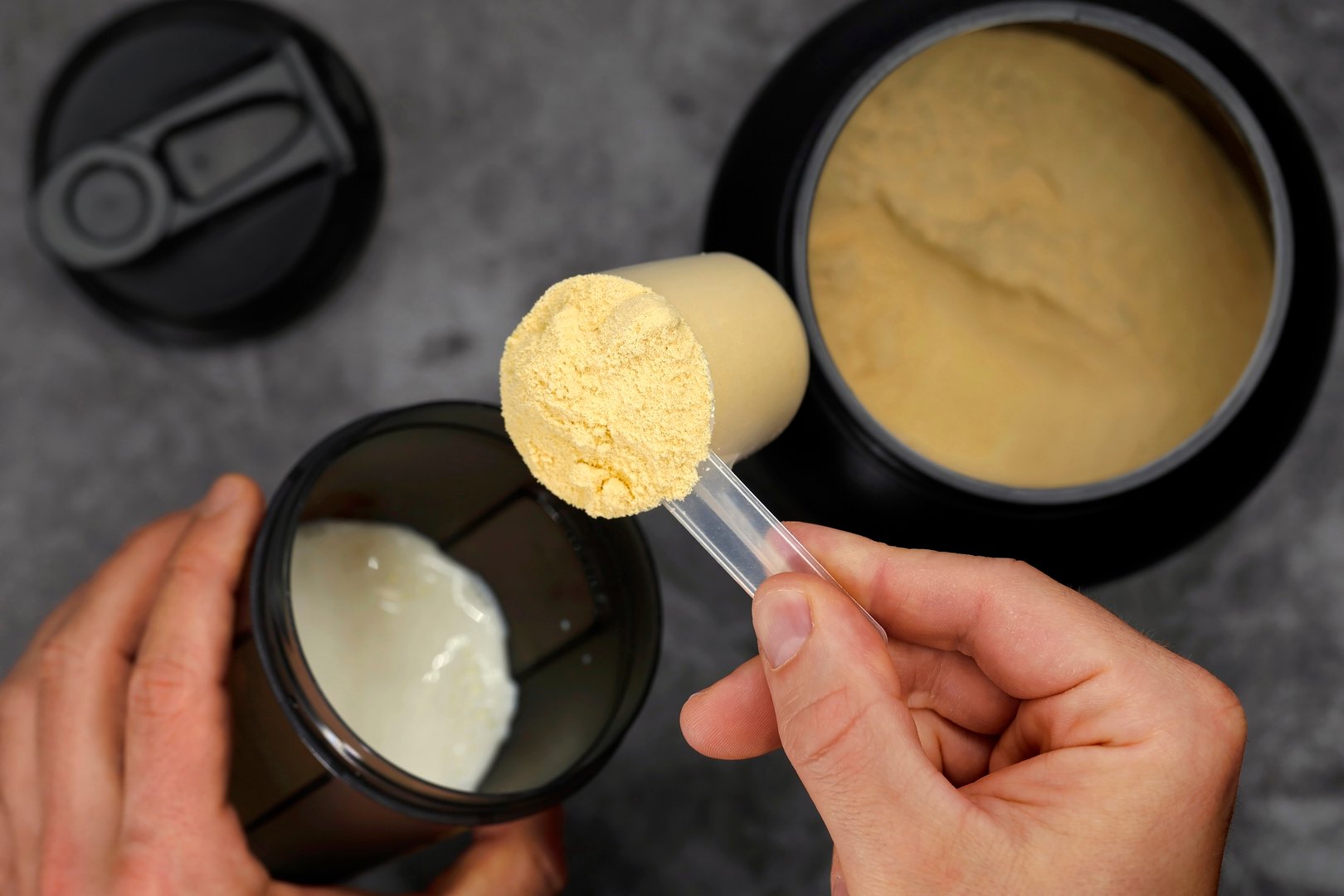 Top view of male hands preparing a protein shake with milk and whey powder in a black shaker, post-workout nutritional supplement for muscle building and faster muscle recovery.
