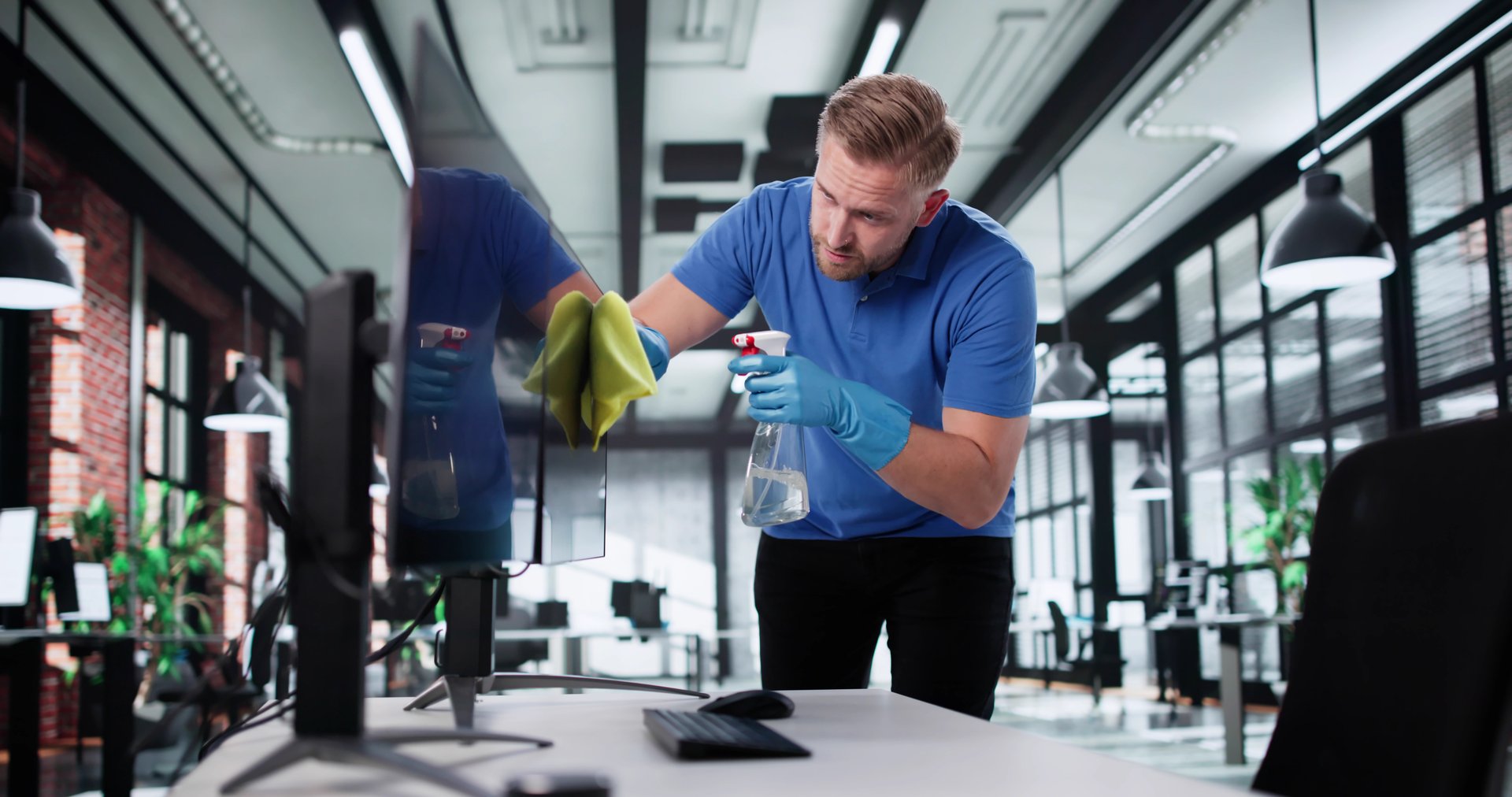 Professional Janitor Cleaning An Office Workspace With Computers And Monitors.
