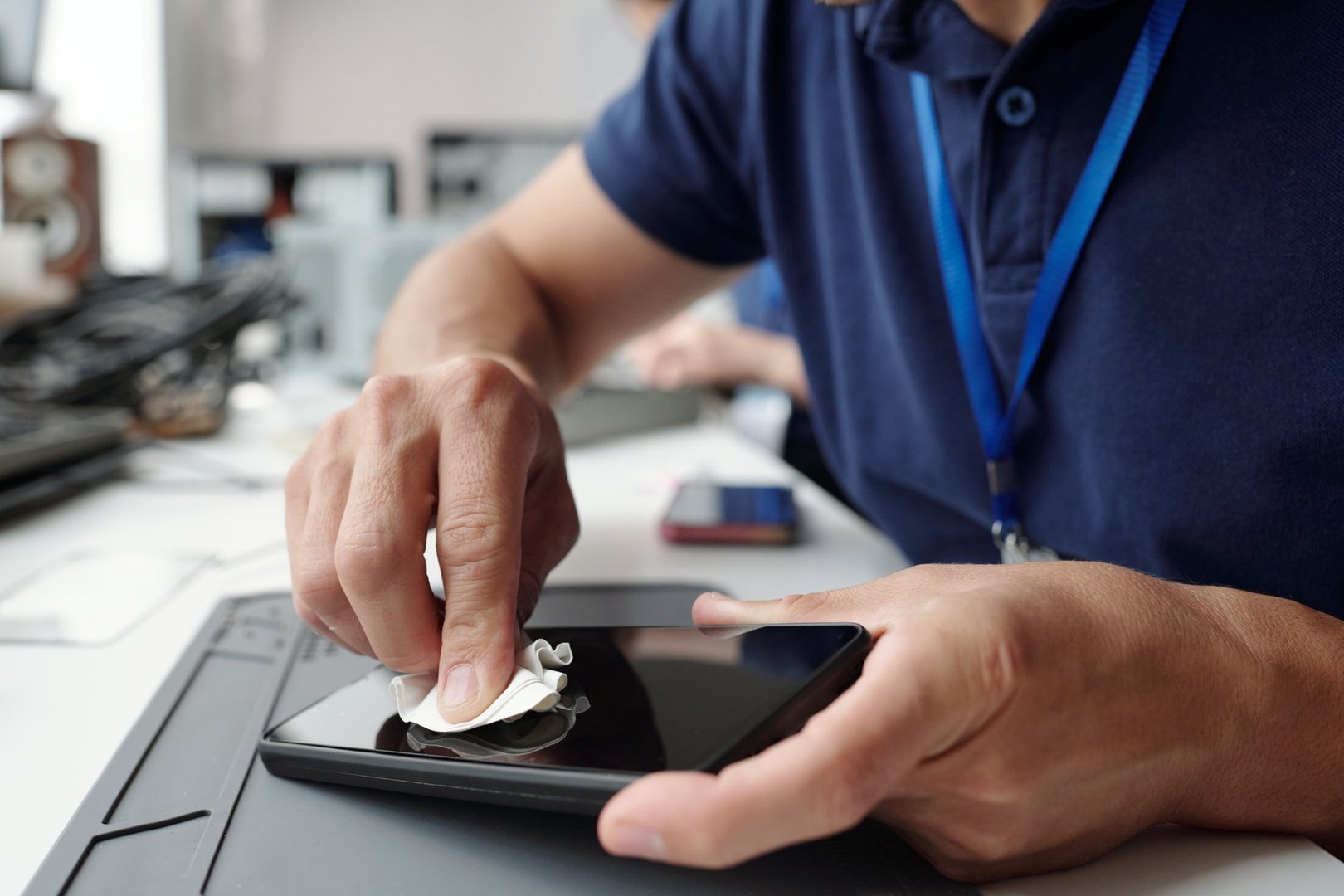 Hands are cleaning tablet screen with cloth in professional office environment. Use of gadget and technology is evident in daily work routine